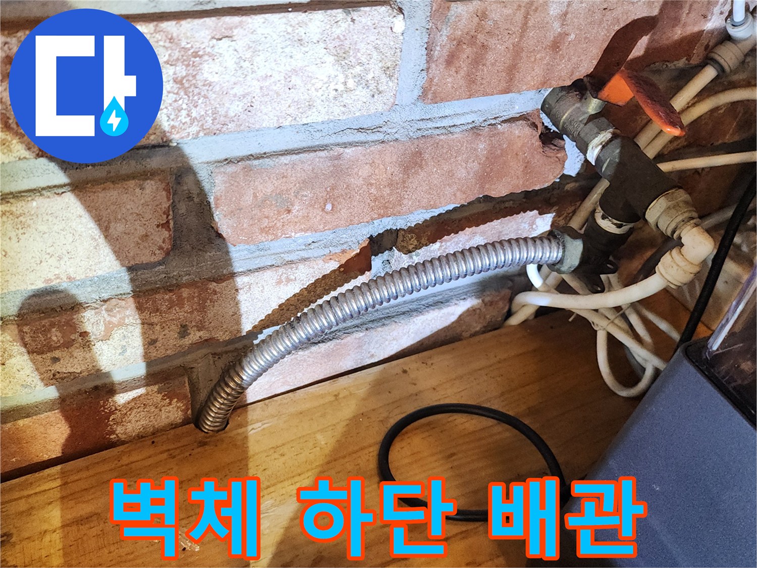 벽돌 벽면 아래에 설치된 금속 주름관과 수도 밸브의 모습