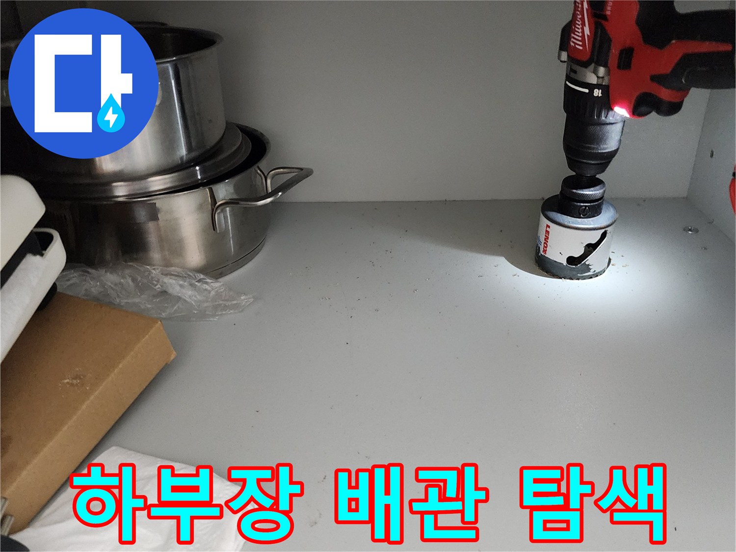 싱크대 하단 선반 근처를 밝게 비추며 누수 지점을 찾는 모습