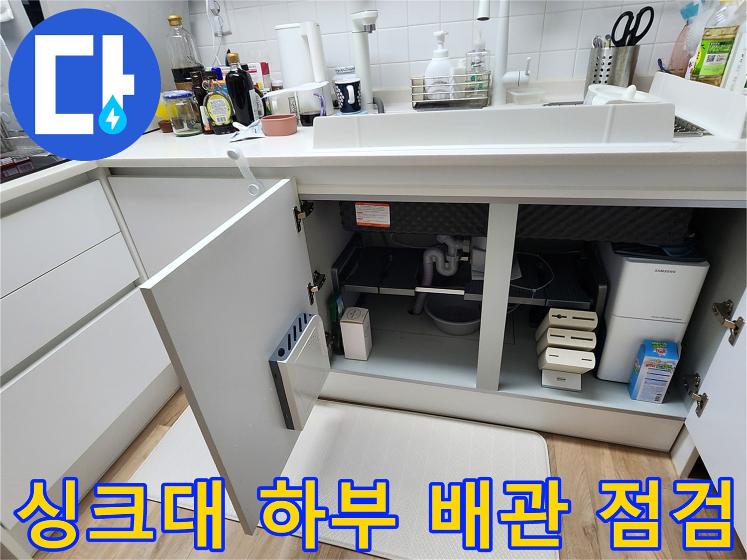 열린 싱크대 하부장 내부의 배수 호스 및 주변 환경 사진
