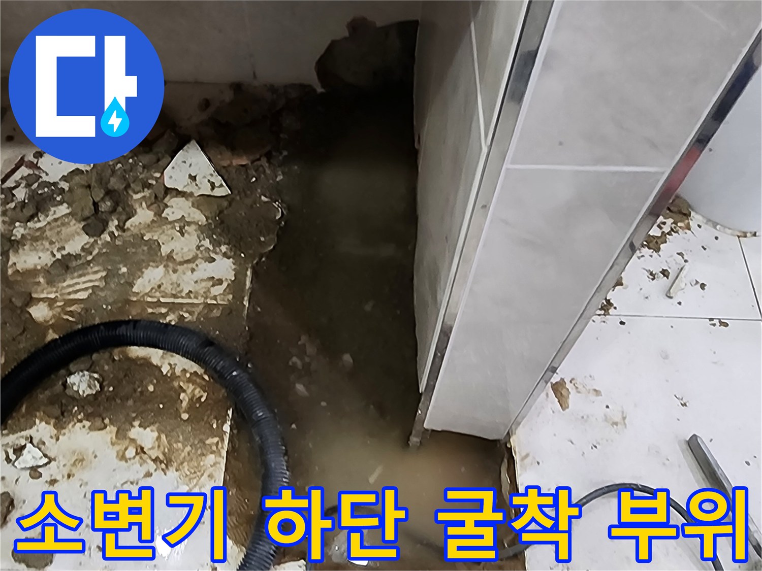 소변기 배관 누수를 확인하기 위해 바닥재를 제거하고 내부를 노출시킨 장면입니다.