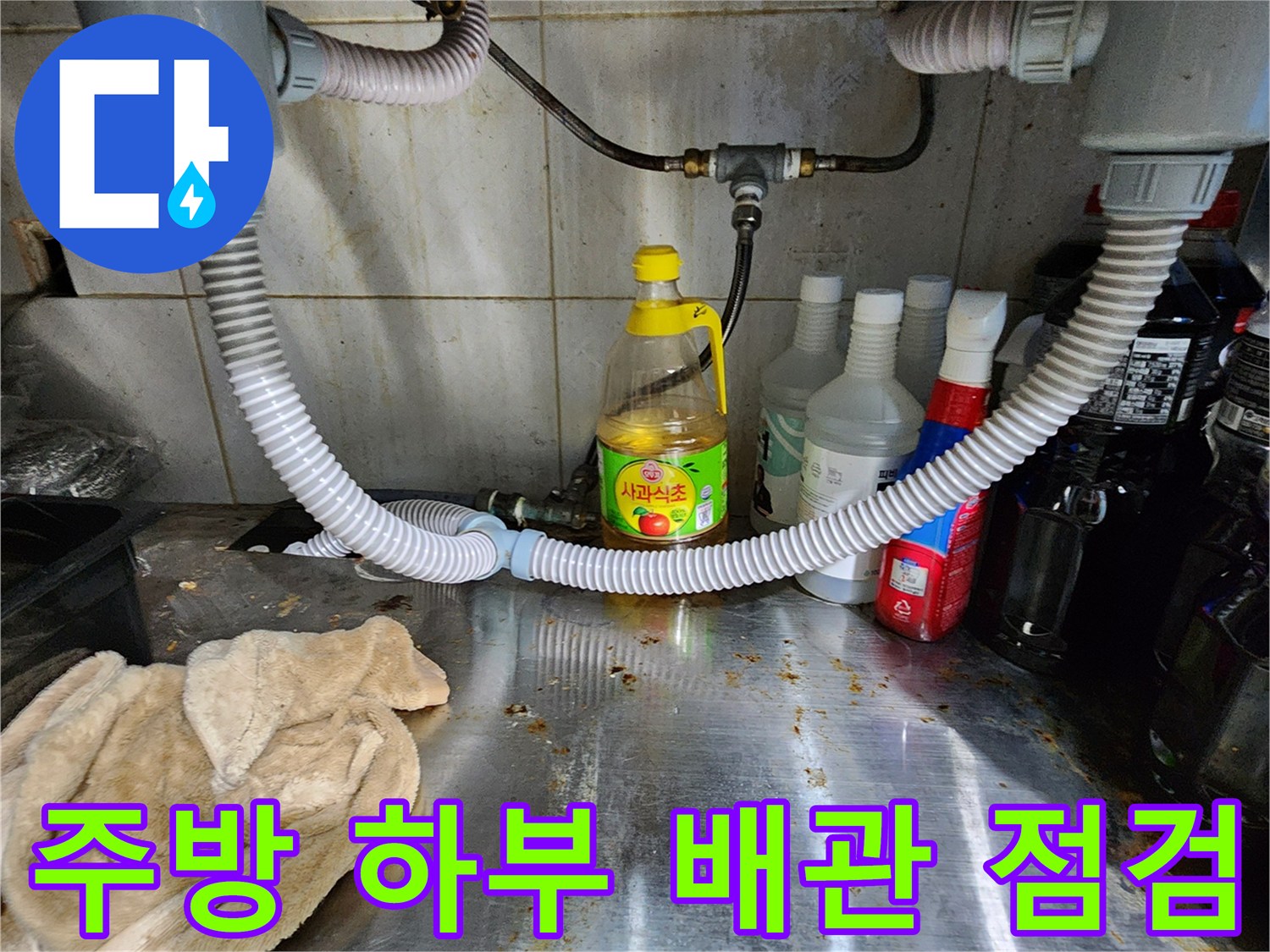 싱크대 밑 배관과 주변 물건들이 놓여 있는 싱크대 하부 모습입니다.