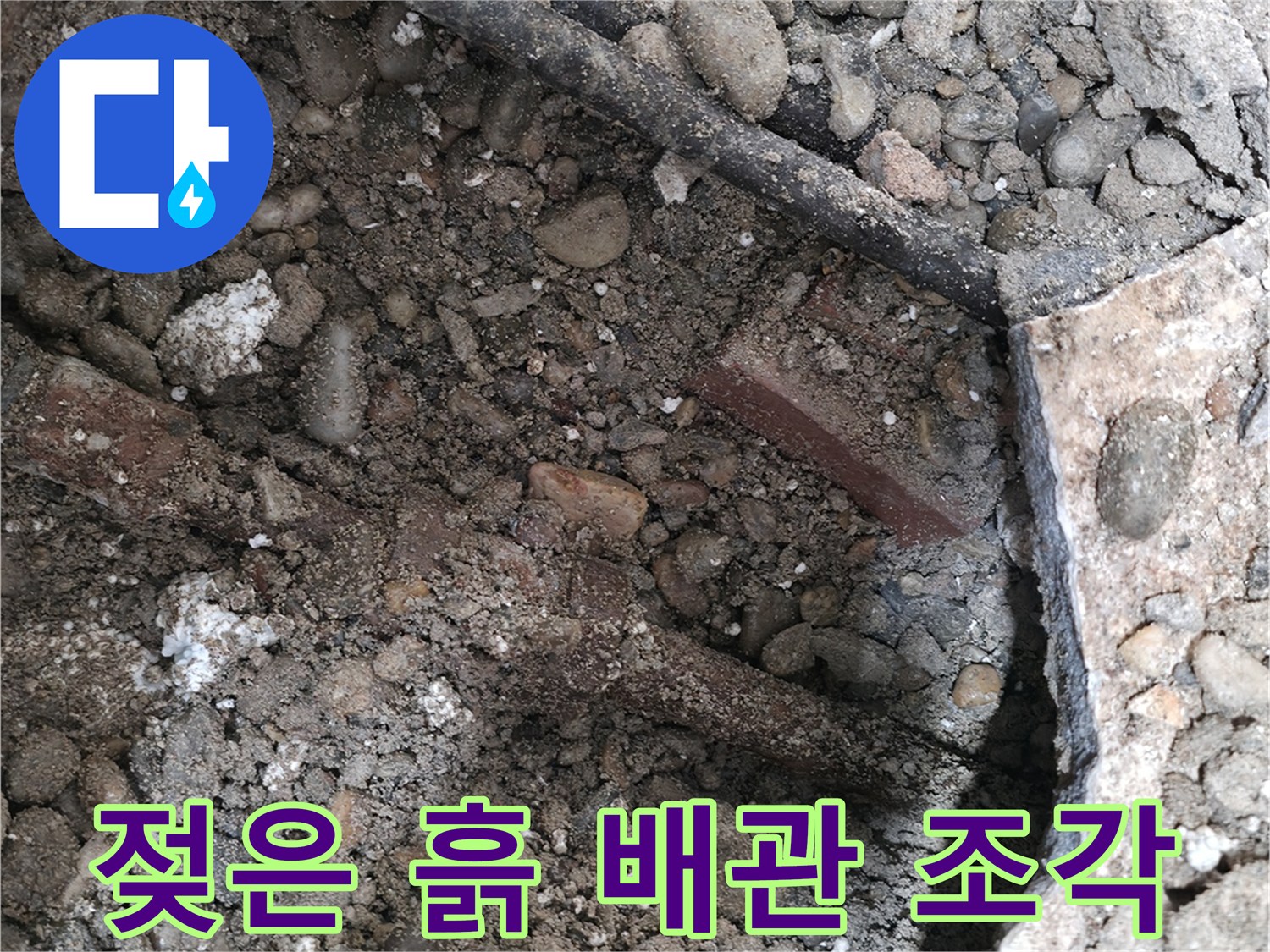 양재동 건물 누수 현장 - 젖은 흙, 낡은 배관 조각, 콘크리트 파편 - 누수의 흔적을 보여줍니다.