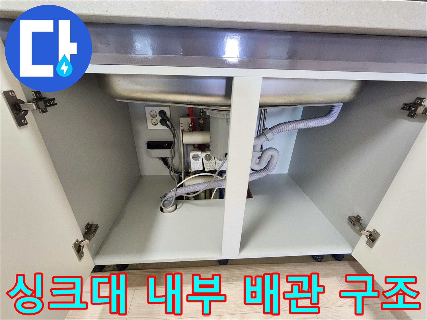 싱크대 아래쪽 배수 호스와 전기 콘센트가 위치한 하부장 내부 모습