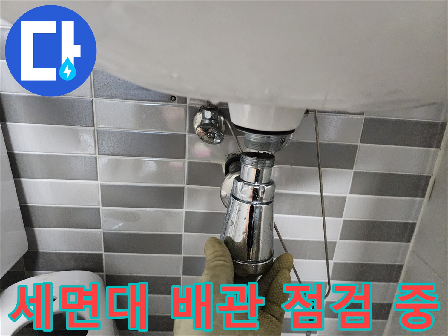세면대 아래쪽 크롬 도금된 배수 트랩을 엔지니어가 손으로 잡고 상태를 확인하고 있습니다.