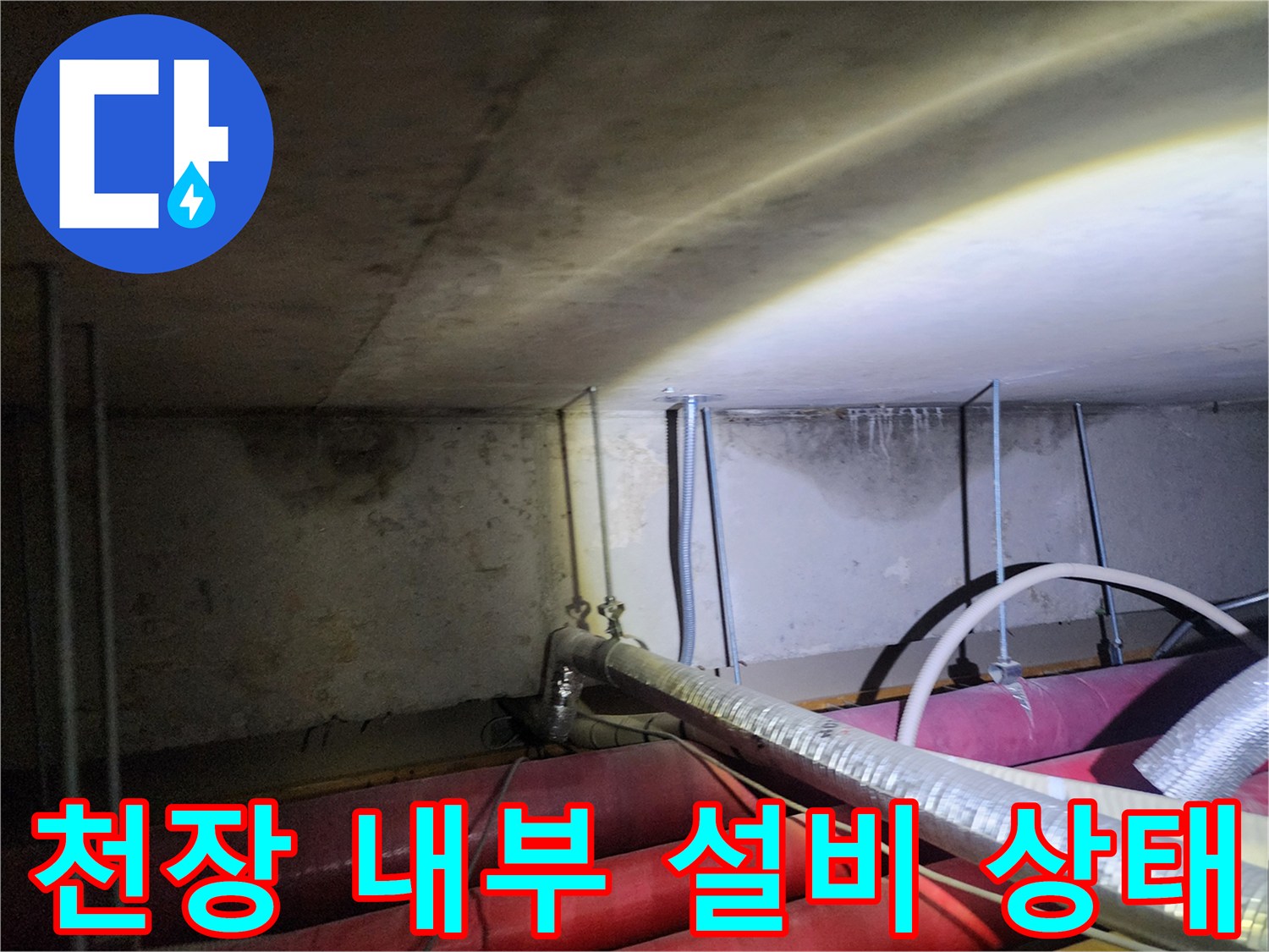 어두운 천장 공간에 설치된 은박 보온재 배관의 모습입니다.