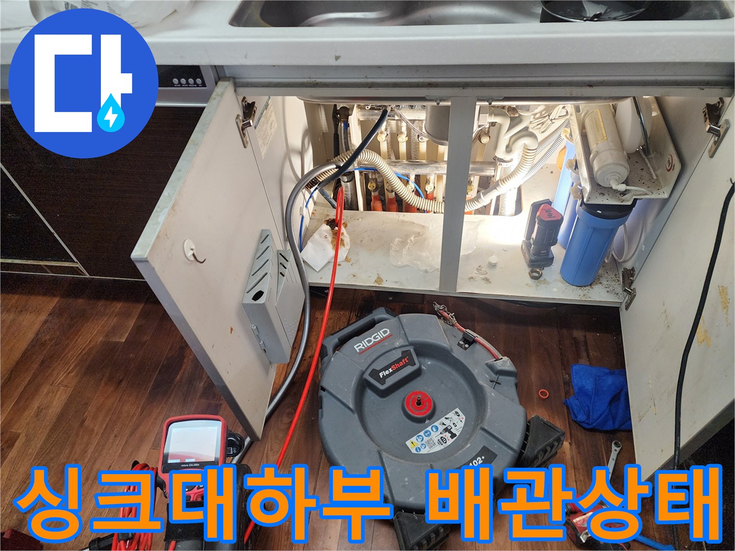 주방 싱크대 하단부의 복잡한 배관과 내시경 장비 모습