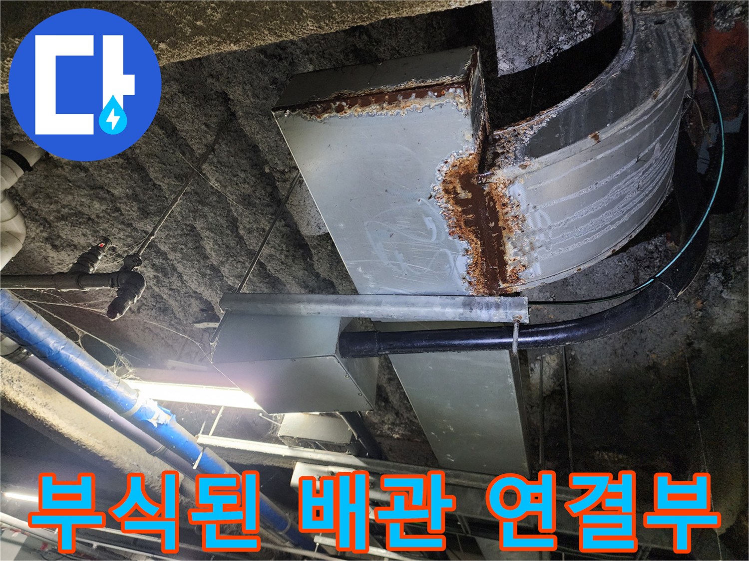 지하 주차장 천장에 설치된 부식되고 녹이 슨 금속 배관의 모습입니다.