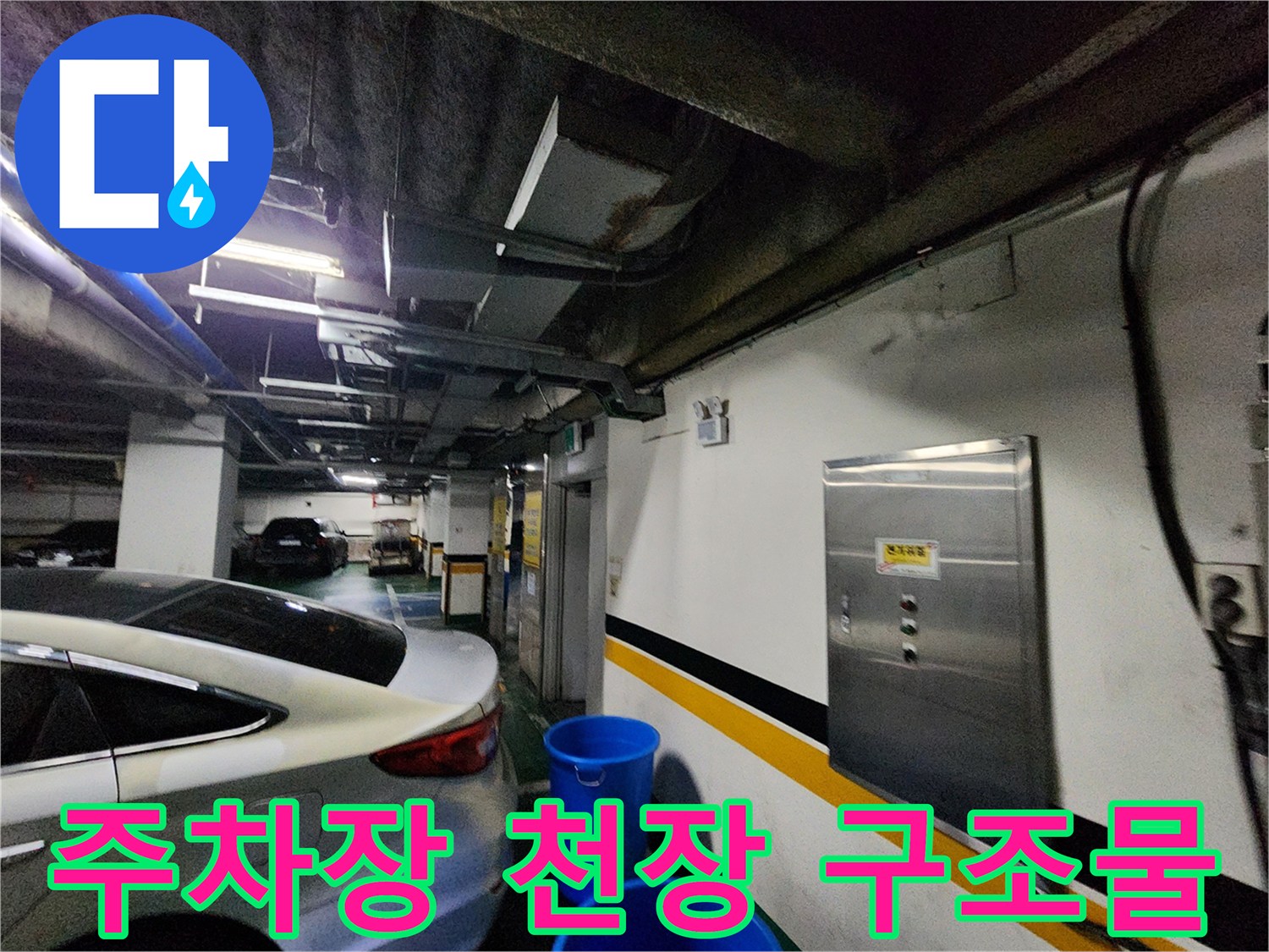 지하 주차장 천장의 노출 배관과 흰색 벽면의 분전함 모습