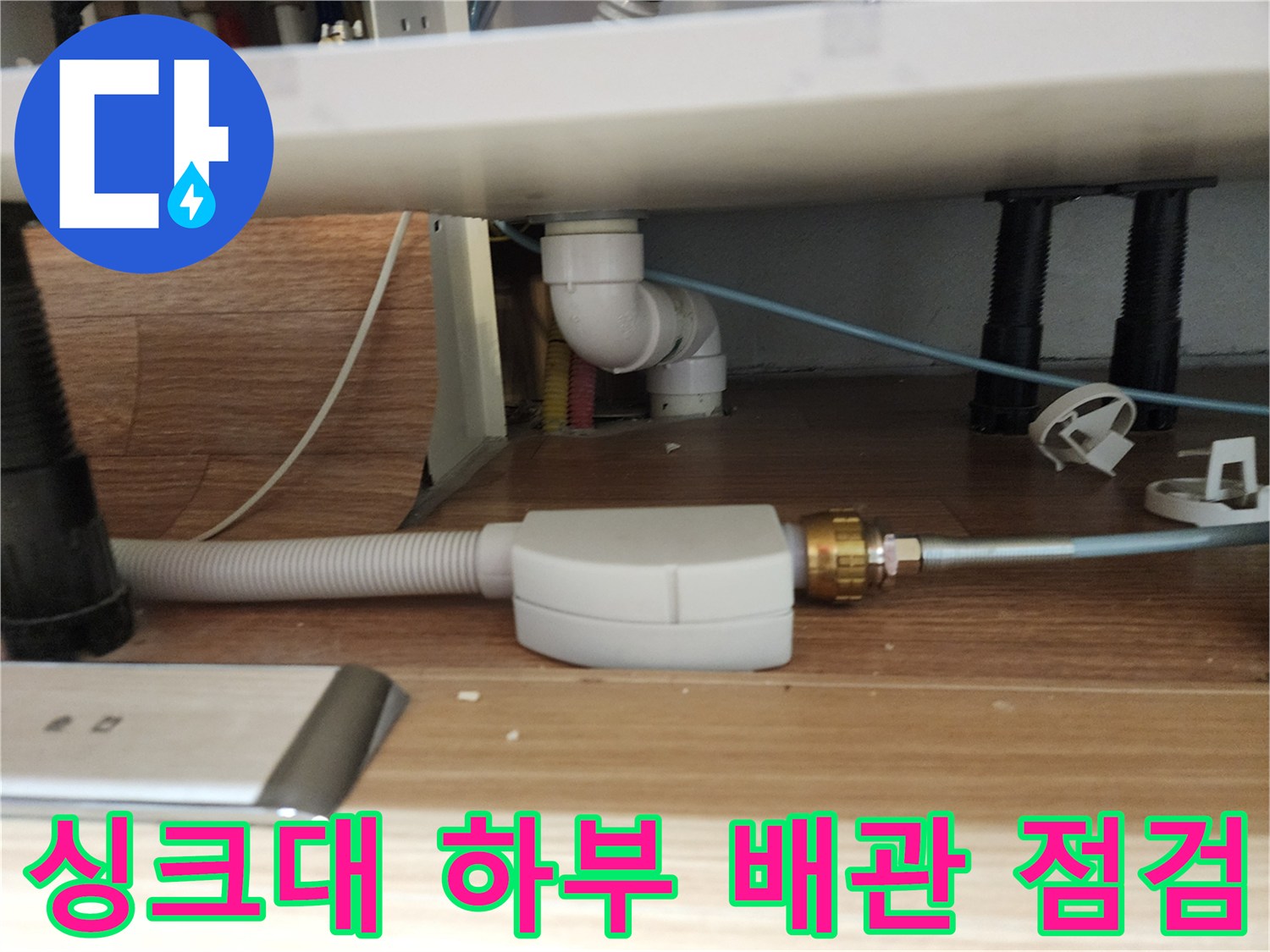 주방 싱크대 아래쪽의 흰색 배관과 연결 부위 모습입니다.