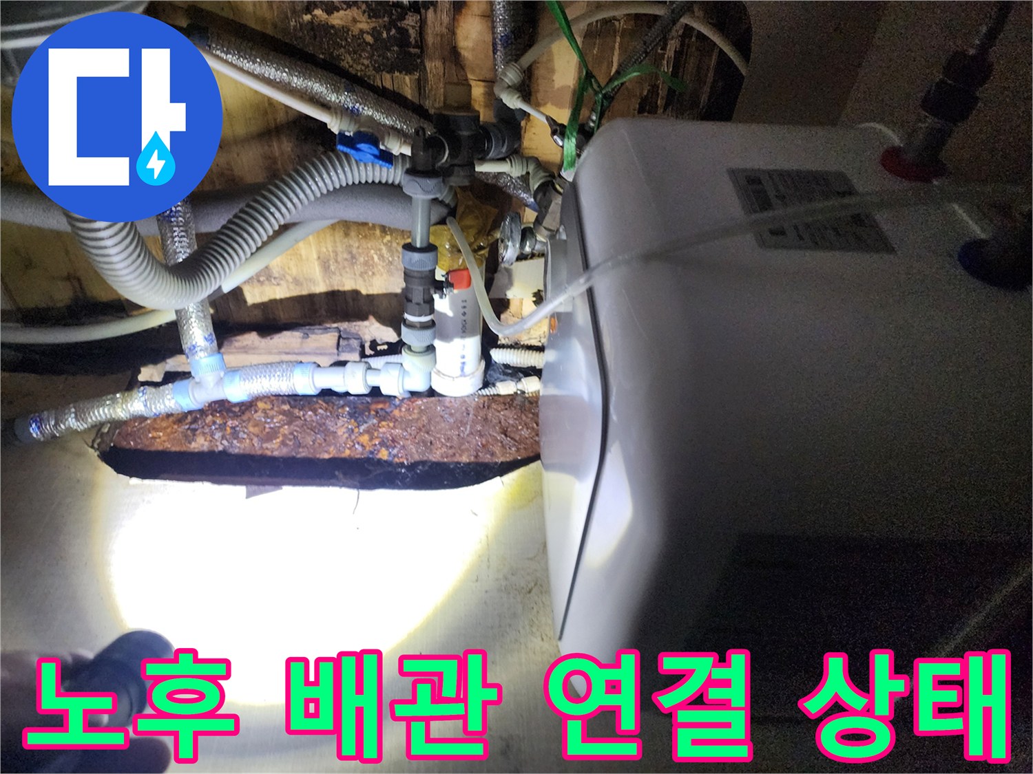 손전등 빛에 드러난 온수기 하단 배관의 부식과 물샘 흔적