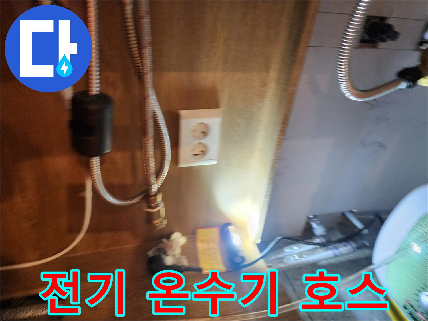 금속 재질의 유연한 배관과 전기 콘센트가 보이는 주방 하부장 내부 전경입니다.