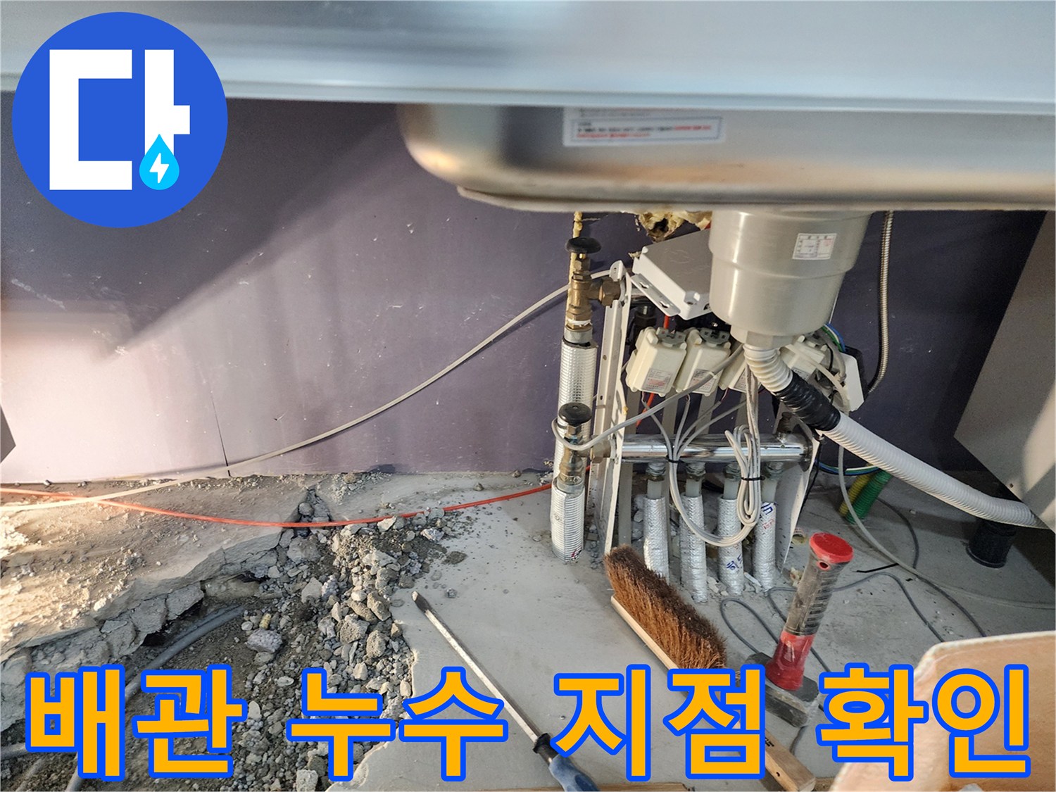 싱크대 하부 공간-노출된 배관과 젖은 바닥 자갈