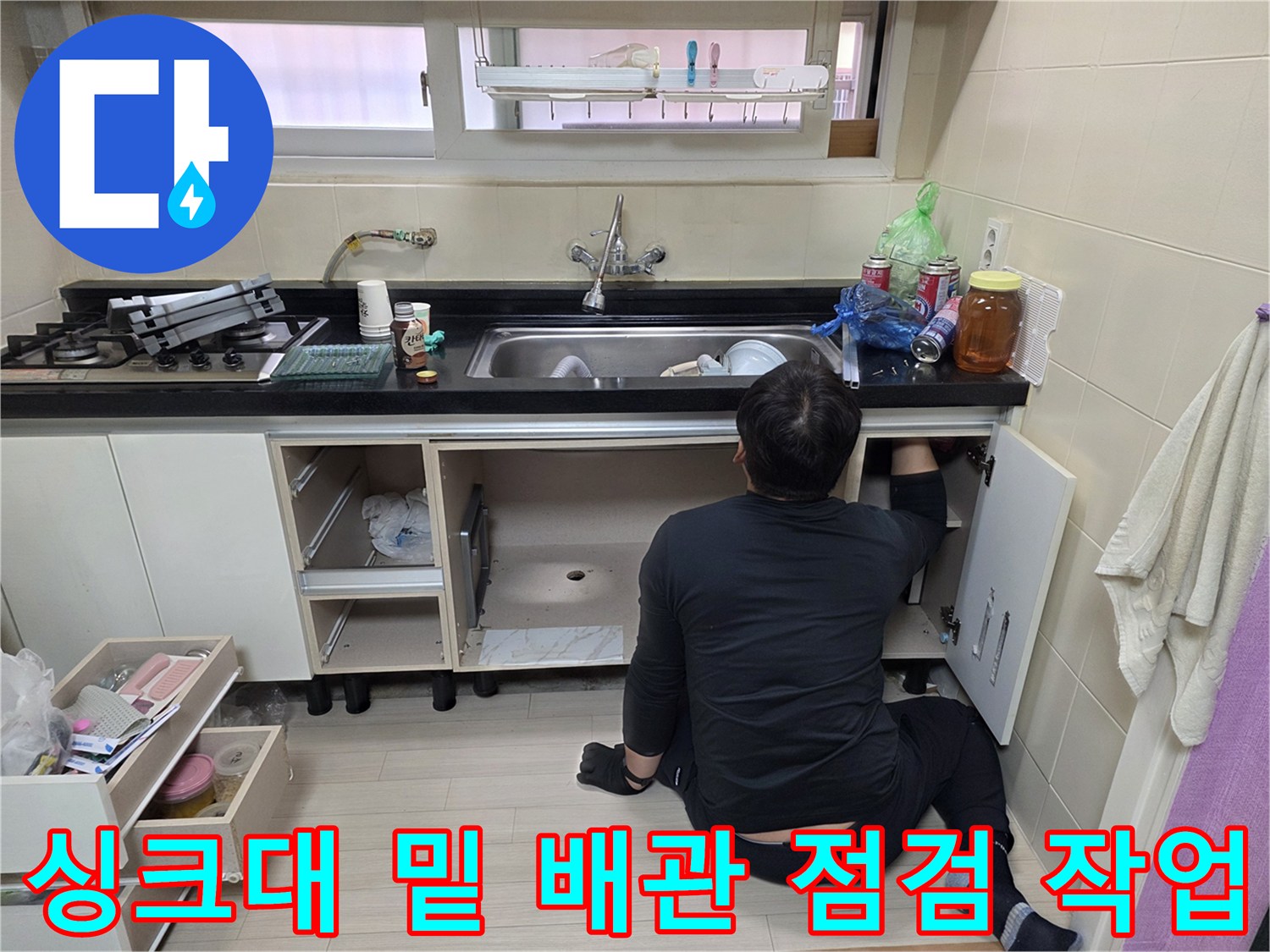 주방 싱크대 아래 공간에서 누수 지점을 찾기 위해 배관을 살피는 모습