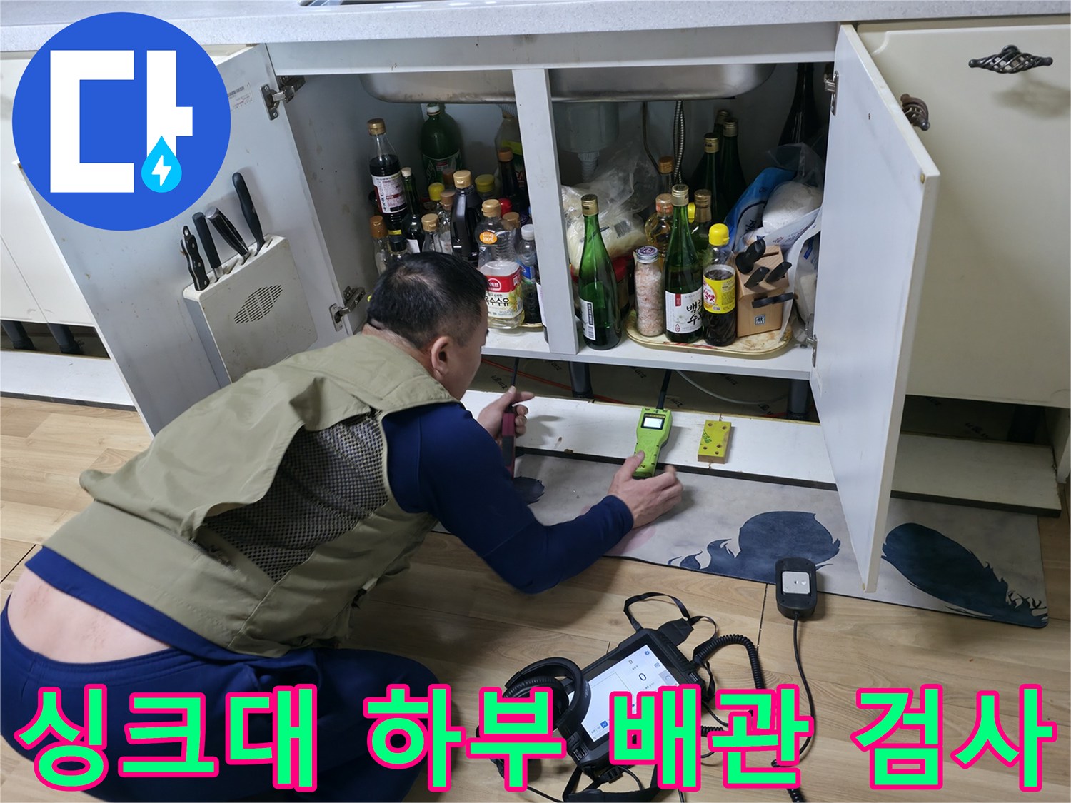 싱크대 하부 수납칸 사이로 탐지 장비를 넣어 배관 상태를 점검하고 있습니다.