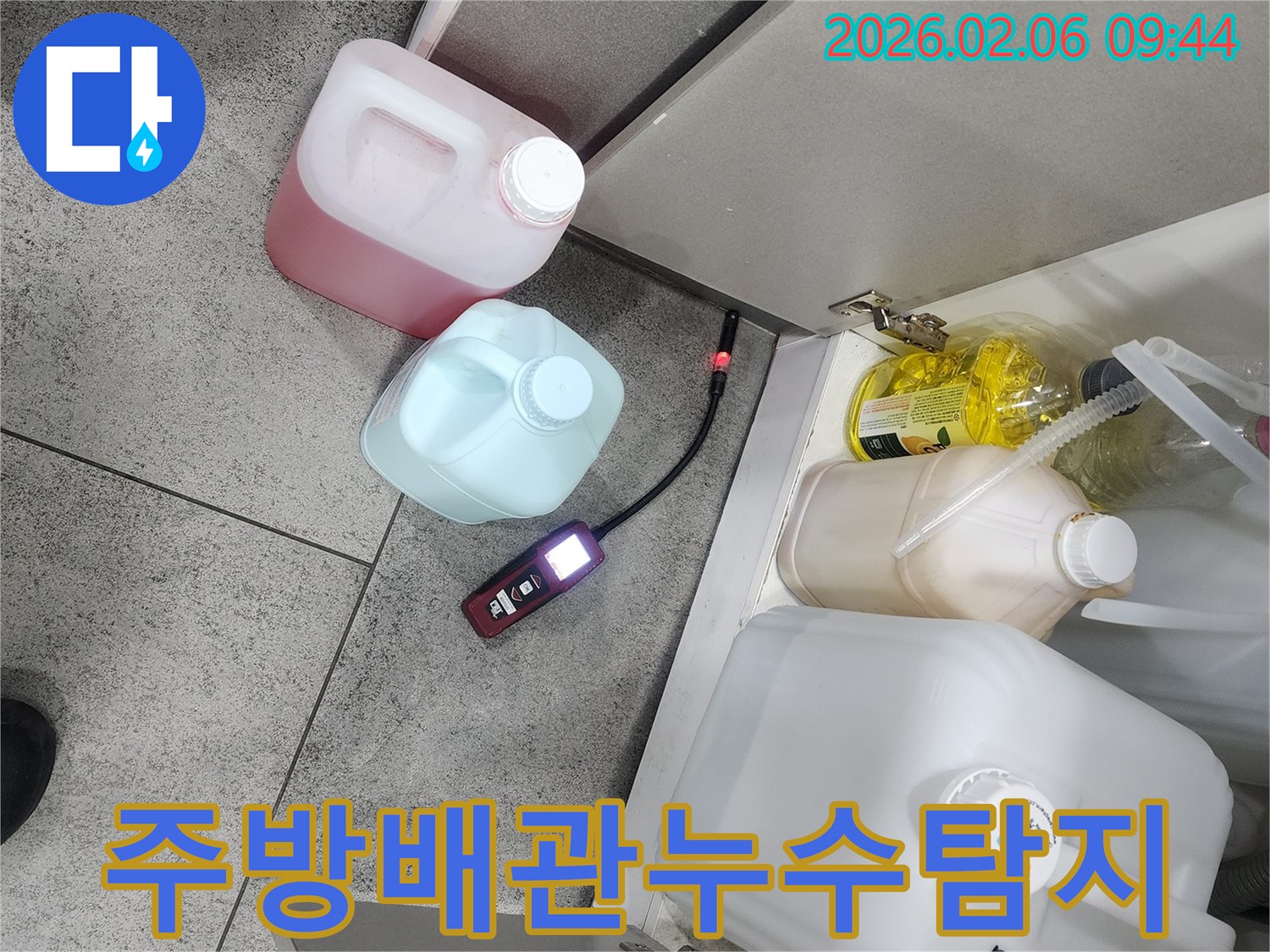 아파트 주방 하부장 아래에서 누수탐지 장비가 배관 누수 위치를 정밀하게 탐지하고 있습니다