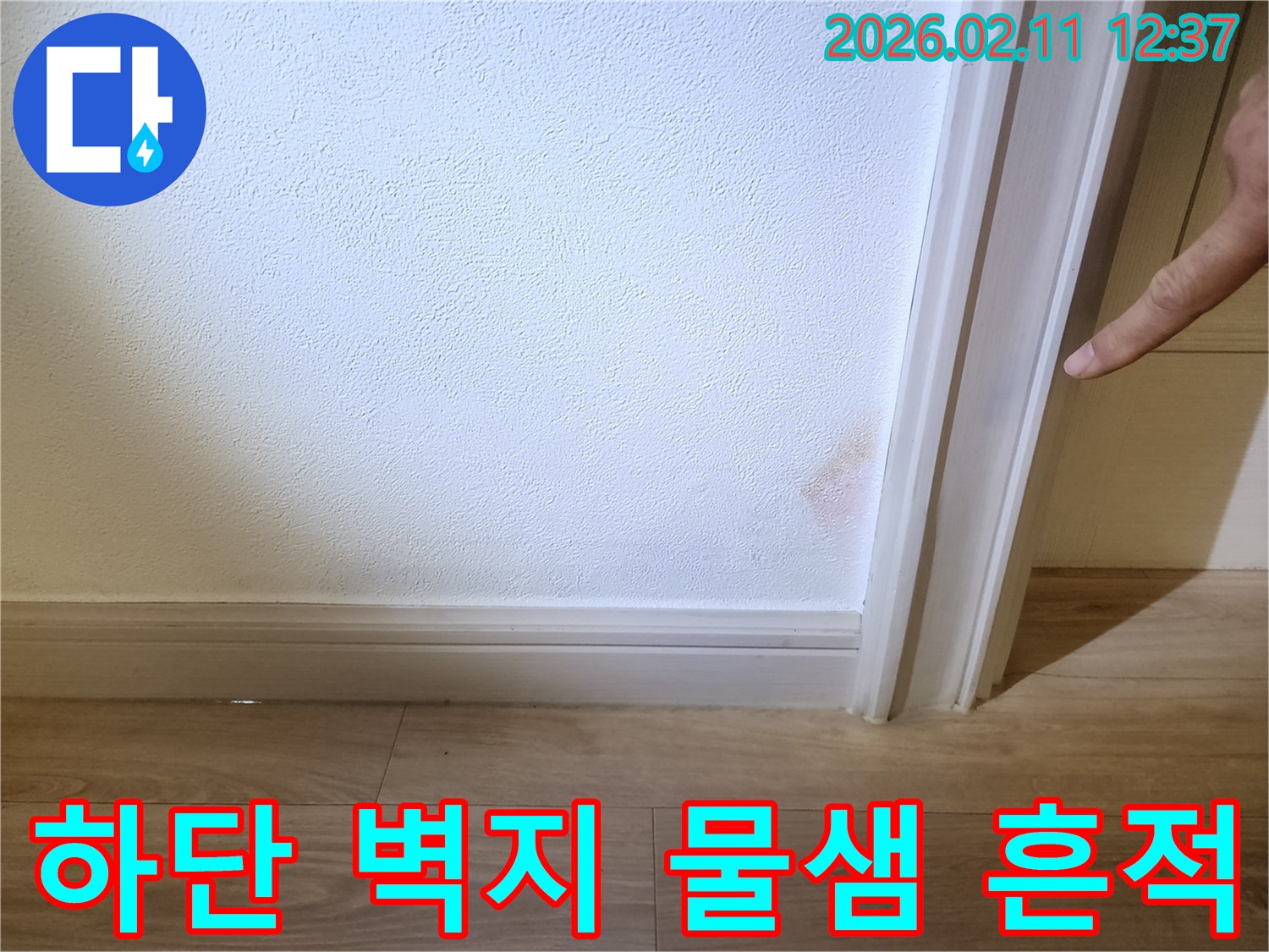 이 사진은 벽 하단에 나타난 물샘 흔적을 보여주며- 벽지가 물에 젖어 색이 변하고 부풀어 오른 상태입니다.