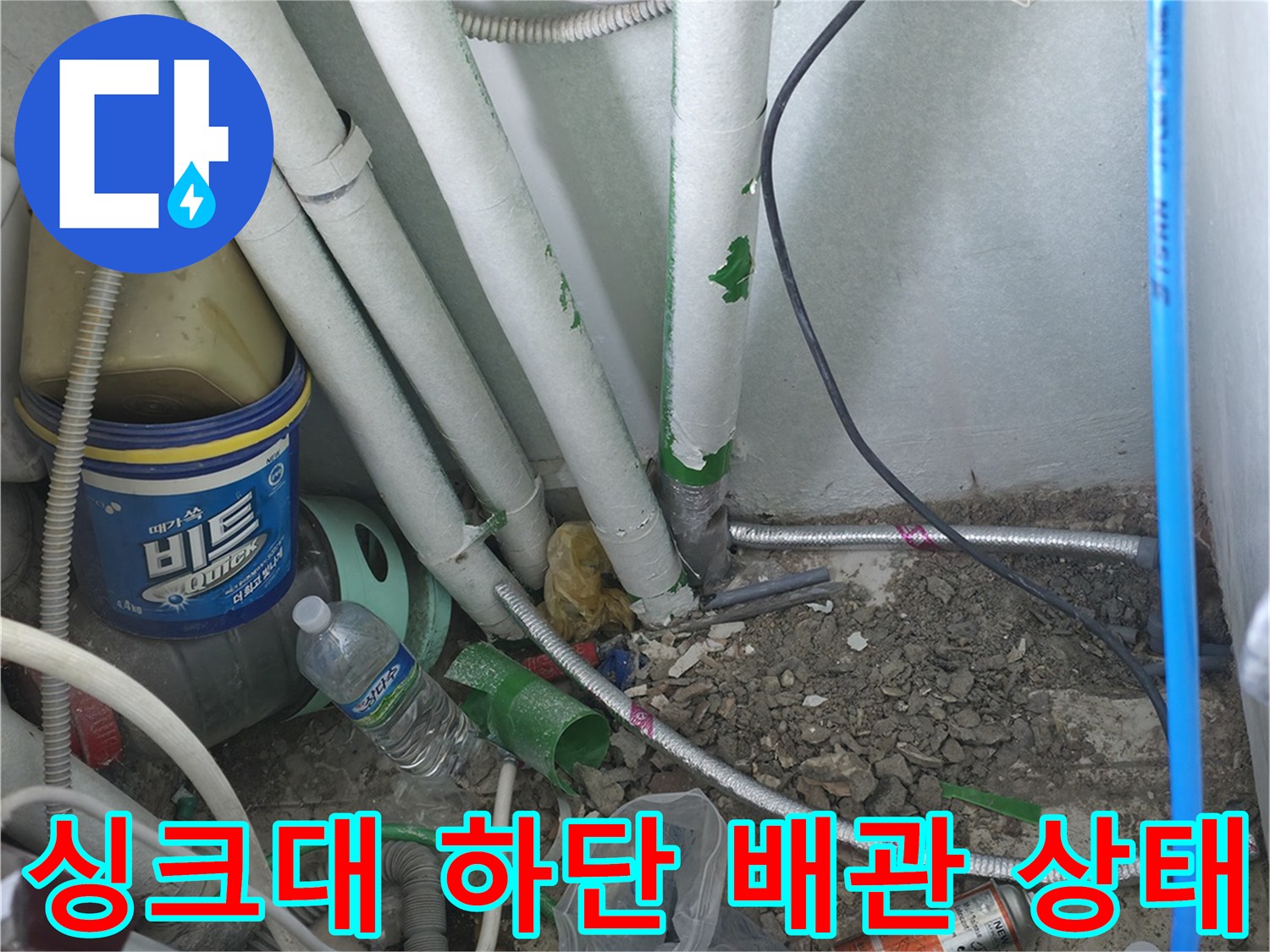 주방 싱크대 아래 복잡한 배관들과 점검 장비가 놓여 있는 현장입니다.
