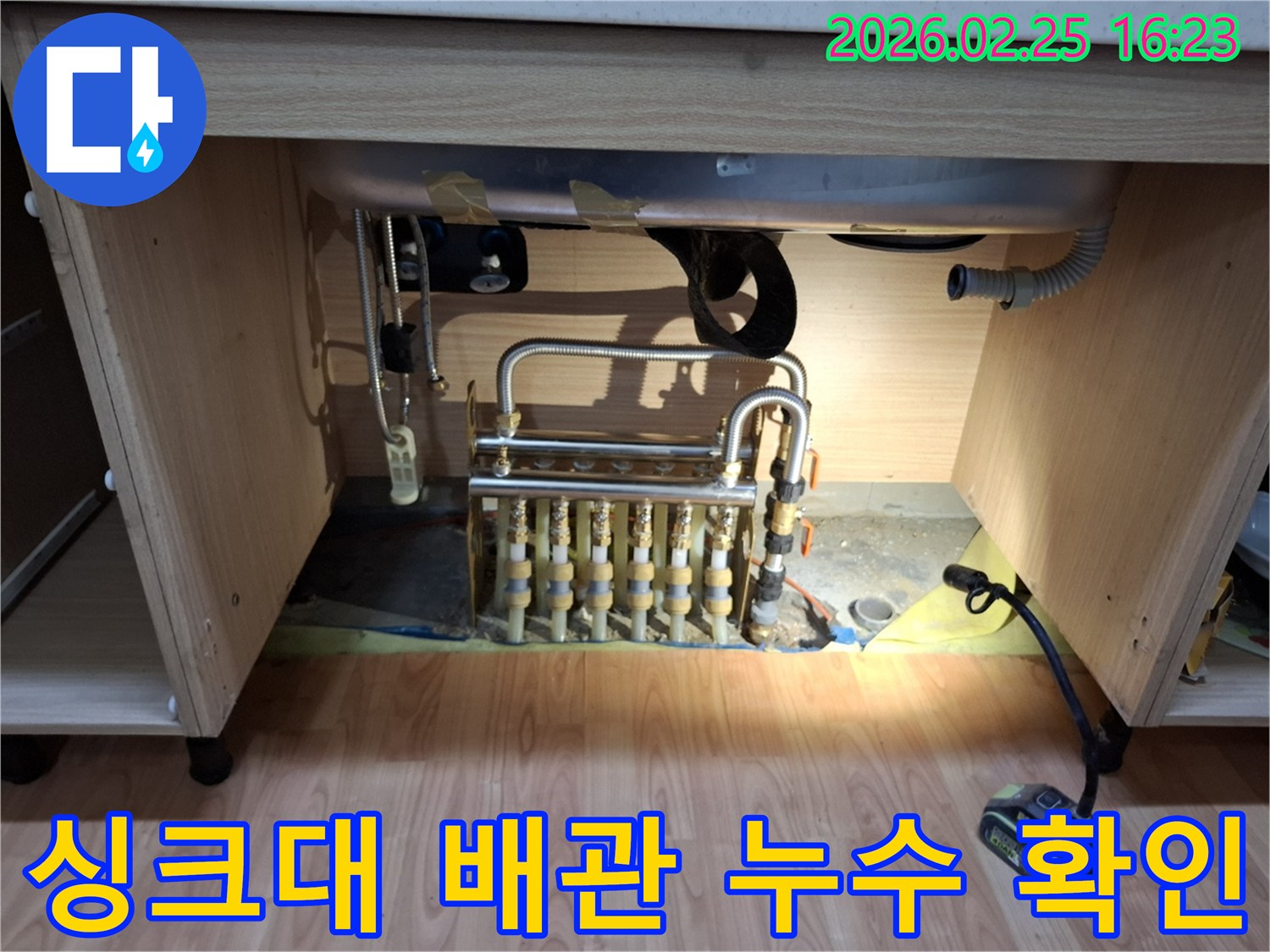 누수 엔지니어가 싱크대 하부의 복잡한 배관 분배기를 정밀하게 점검하고 있습니다.