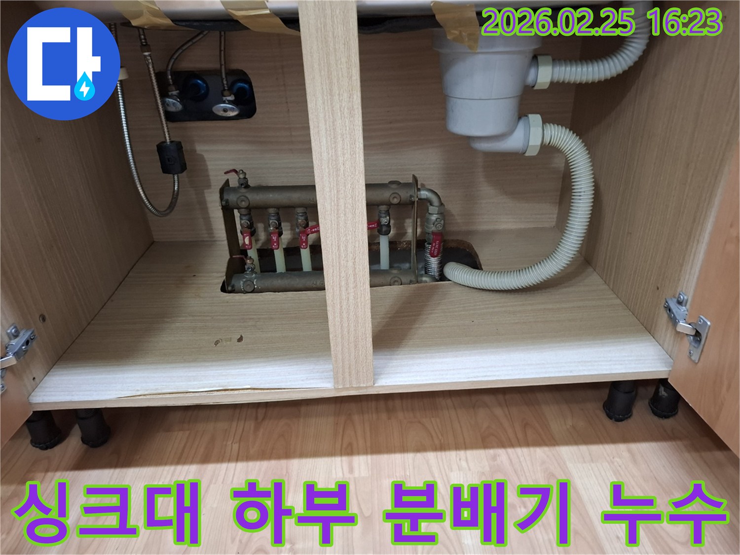 싱크대 하부장 아래에 설치된 보일러 분배기에서 발생한 누수-현장을 촬영한 이미지입니다