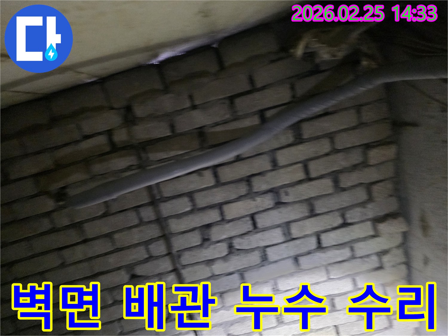 어두운 벽돌 벽면을 배경으로-단열재로 감싸인 배관과-다른 배선이 누수 여부를-확인하기 위해 촬영된 현장 이미지입니다.