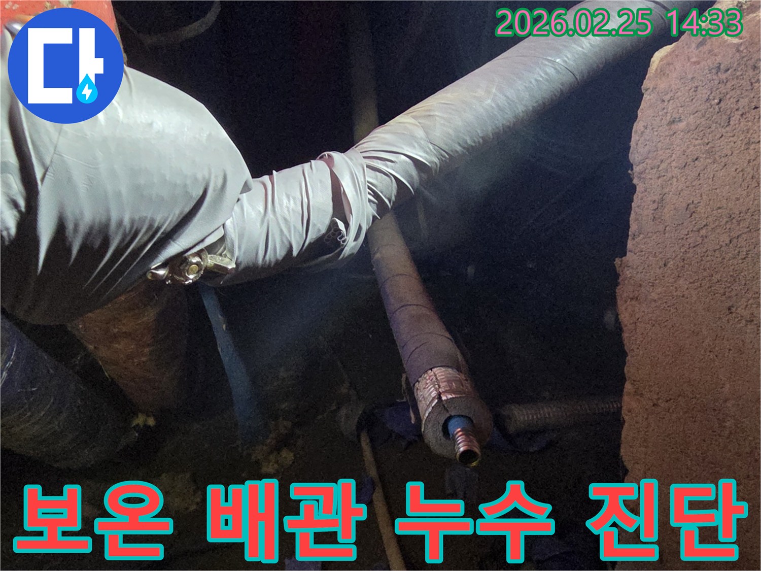 어두운 작업 공간에서-장갑을 낀 손이-보온재로 감싸진-배관의 손상 부위를-세심하게 점검하며-누수 원인을-진단하는 모습입니다