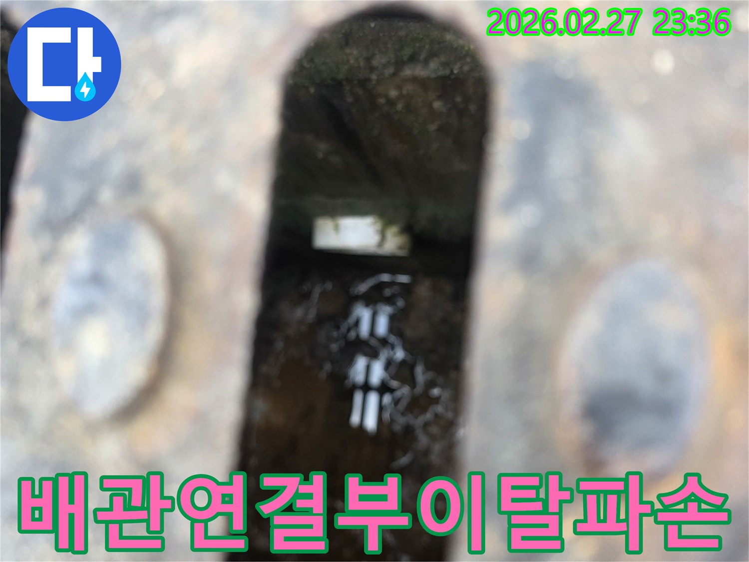 녹슨-철제-격자-아래-어두운-공간에-고인-물과-이탈된-듯한-배관-연결부가-보이는-누수-현장