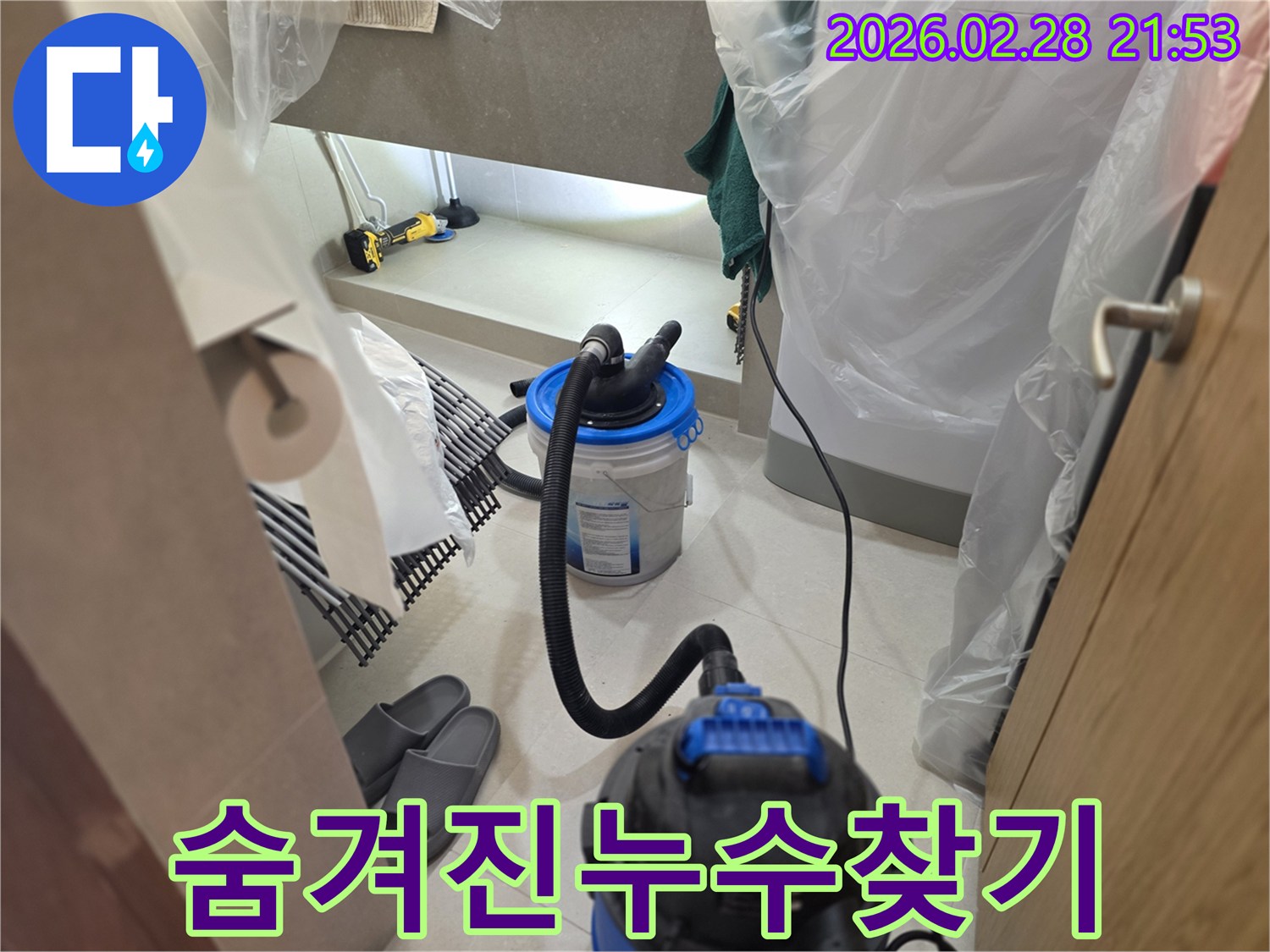 이 이미지는 누수 현장에서-주변을 비닐로 보양하고-습식 청소기와 조명 장비를 사용하여-숨겨진 누수 지점을 찾아내는 대작전을 보여줍니다.