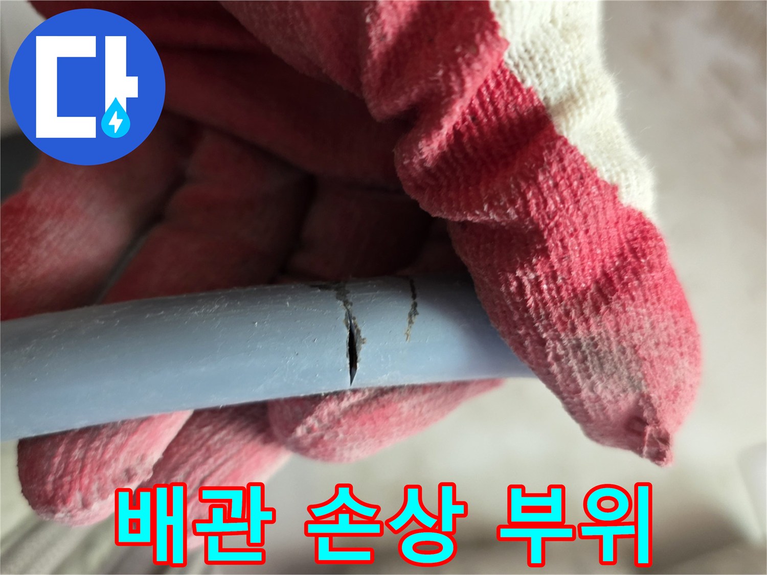 작업용 장갑을 낀 손이 잡고 있는 균열된 파란색 배관
