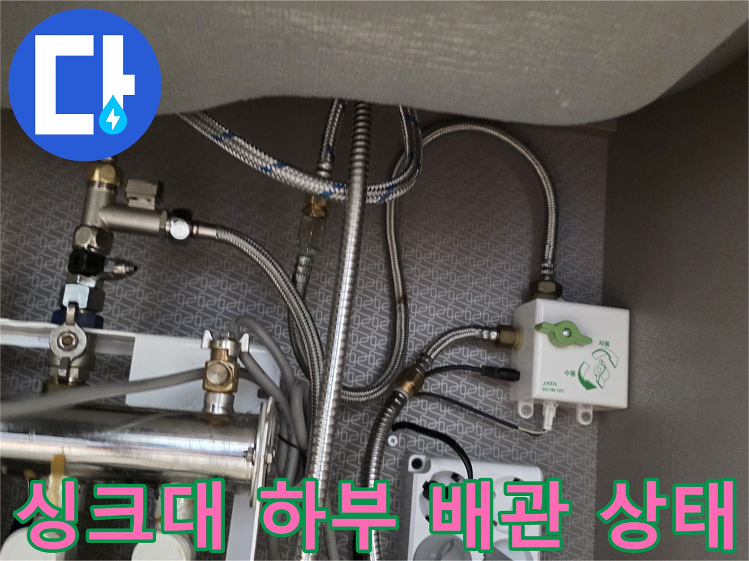 주방 싱크대 아래쪽의 복잡한 금속 배관과 연결 부위 모습입니다.