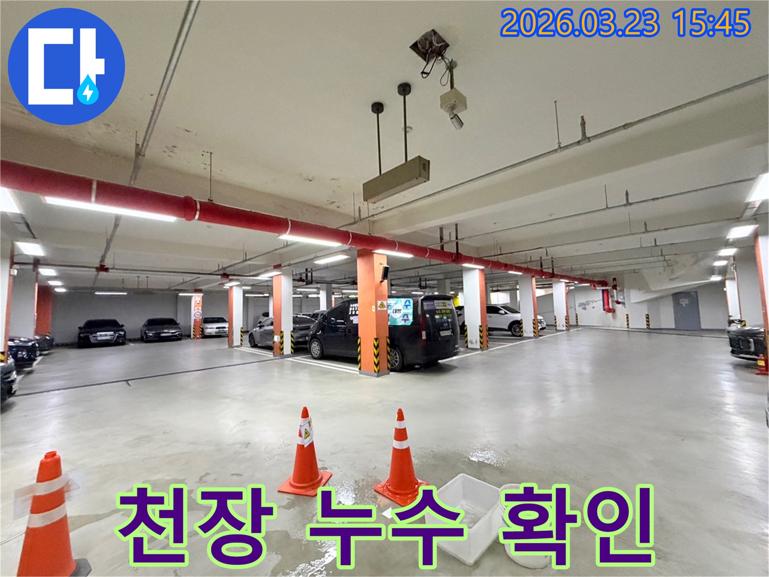 지하 주차장 천장에서 물이 새어-바닥에 고인 물과 안전 조치들을 보여주는-누수 현장 사진입니다