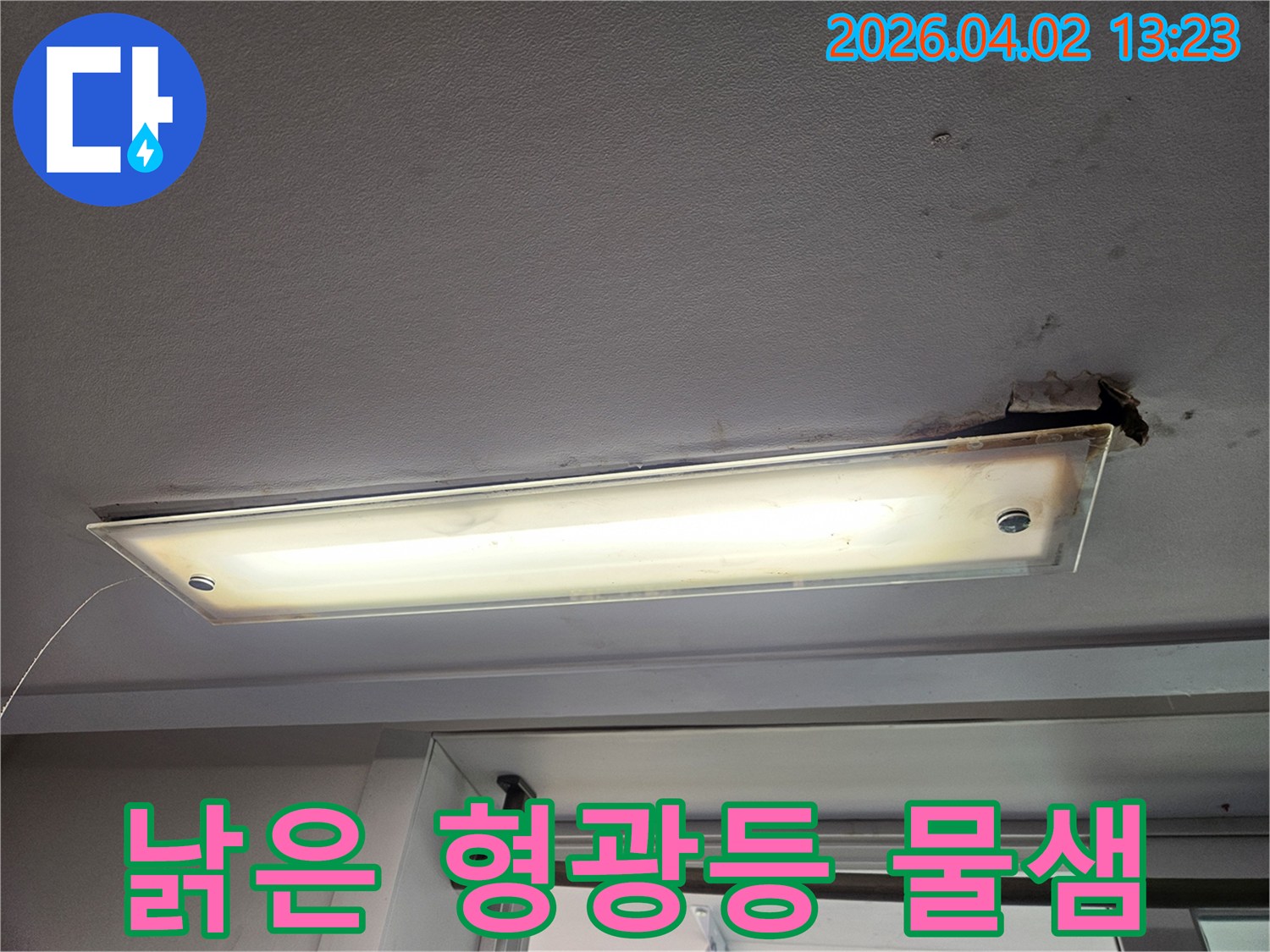 오래된 형광등 주변으로 물샘 자국과 함께 천장 마감재가 손상된 누수 현장을 보여주는 이미지