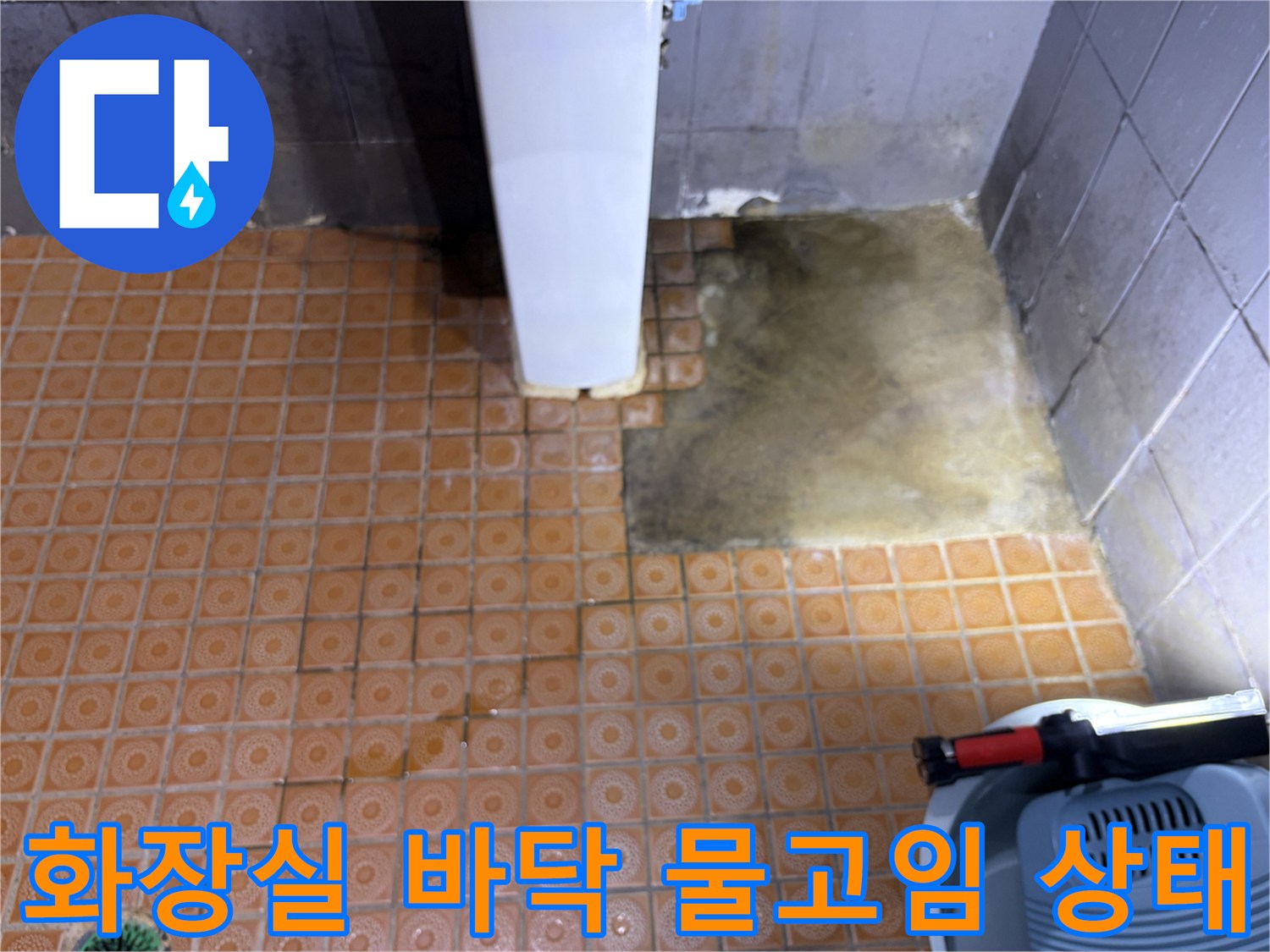세면대 옆 화장실 바닥 타일에 물이 고여 있고 습기가 가득한 모습입니다.