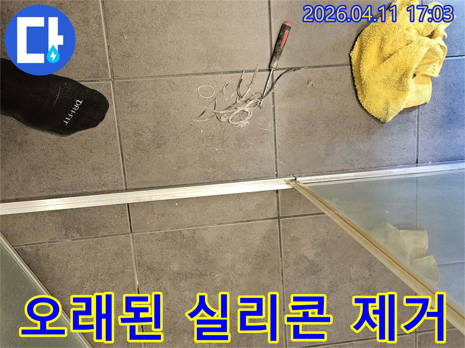 욕실 바닥에 놓인 노란 걸레와-공구-그리고 샤워부스 주변의 낡은 실리콘을 제거하는 작업 현장