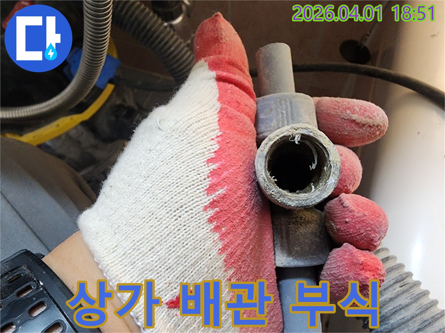 작업용 장갑을 낀 손으로-상가 건물 내 부식된 배관을 들고-신속한 교체의 중요성을 설명하는 모습