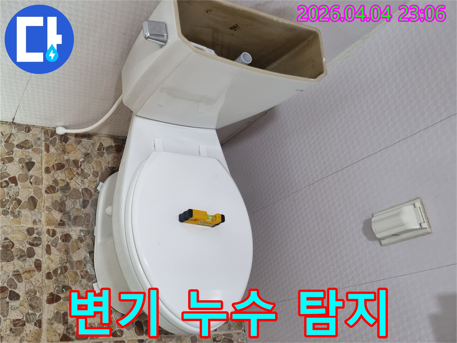 변기 물탱크가 열려 내부 부품이 노출된 상태로-수평계가 변기 시트 위에 놓여-누수 탐지 작업이 진행되고 있습니다