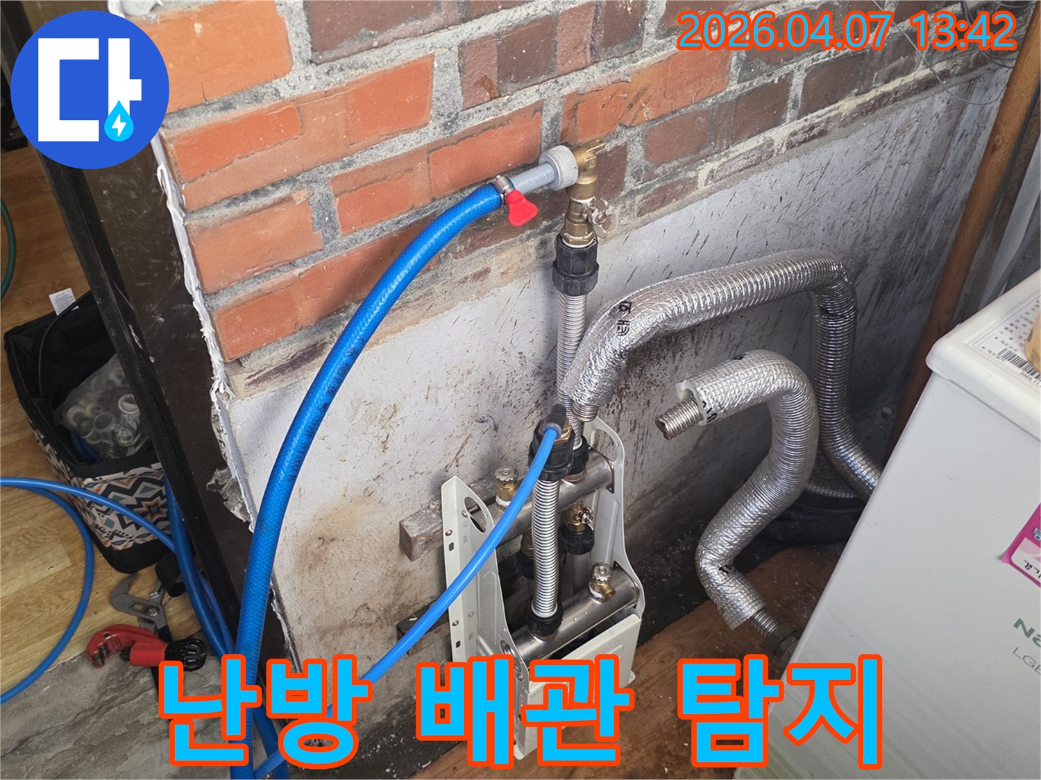 벽돌 벽 옆에-난방 배관과-연결된 누수 탐지 장비가-설치되어 있으며-정확한 누수 지점을 찾기 위한-초기 작업이 진행 중입니다.