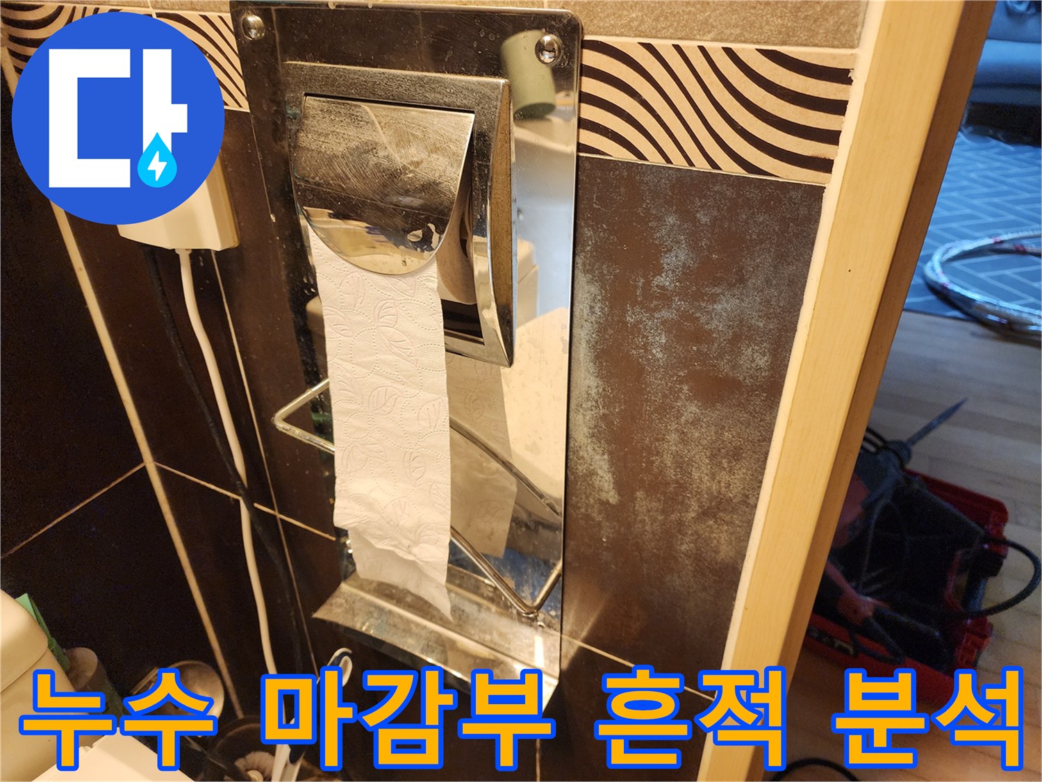 화장실 분배기 마감부-주변의 타일 벽면에-나타난-오래된-누수 흔적과-오염 상태를-보여주는-이미지입니다.