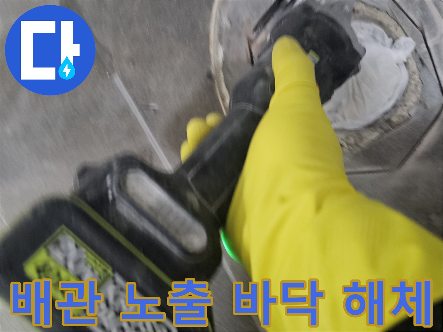 노란색 작업 장갑을 착용한-전문가가-전동 공구로-오수 배관 주변의 바닥 타일을-세심하게 제거하여-배관을 노출시키는 과정입니다.
