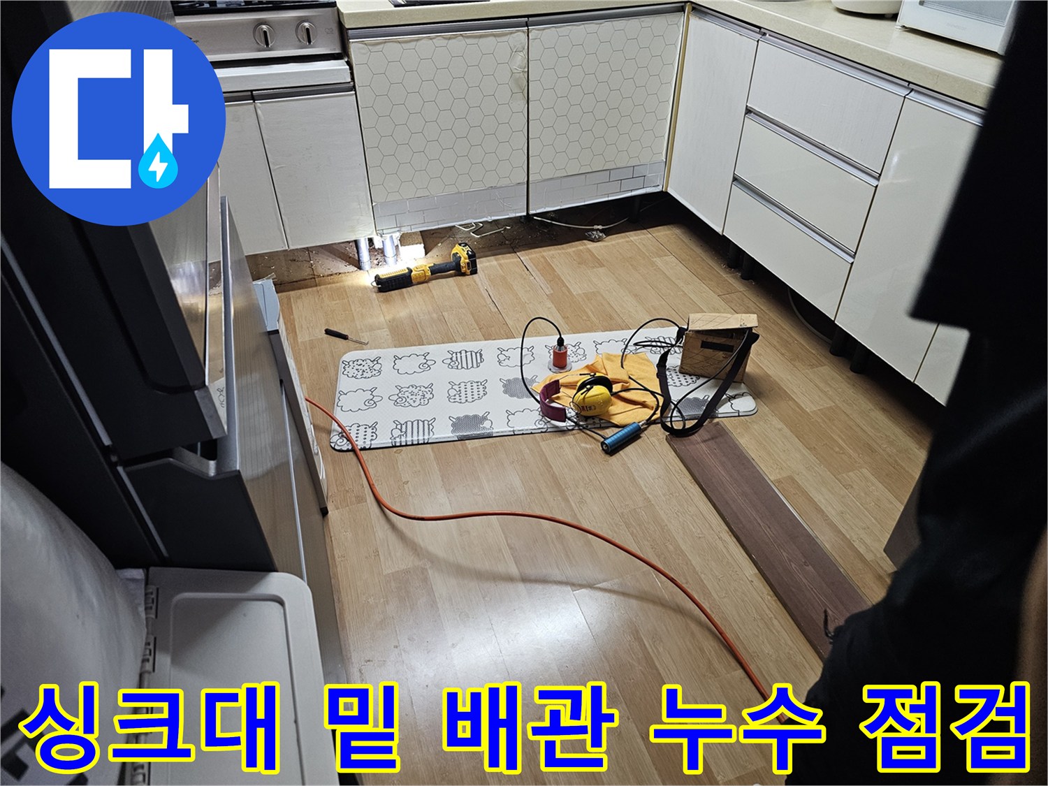열려 있는 싱크대 하부 공간과 바닥에 배치된 작업 도구들