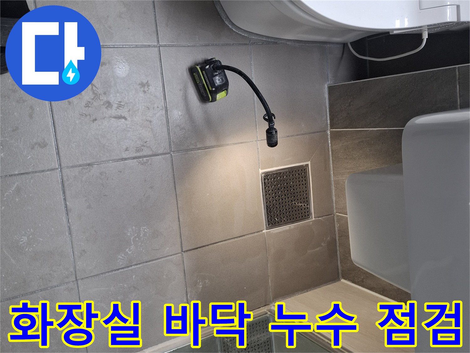 변기 옆 배수구 주변의 타일 상태와 장비 설치 모습을 보여주는 사진입니다.