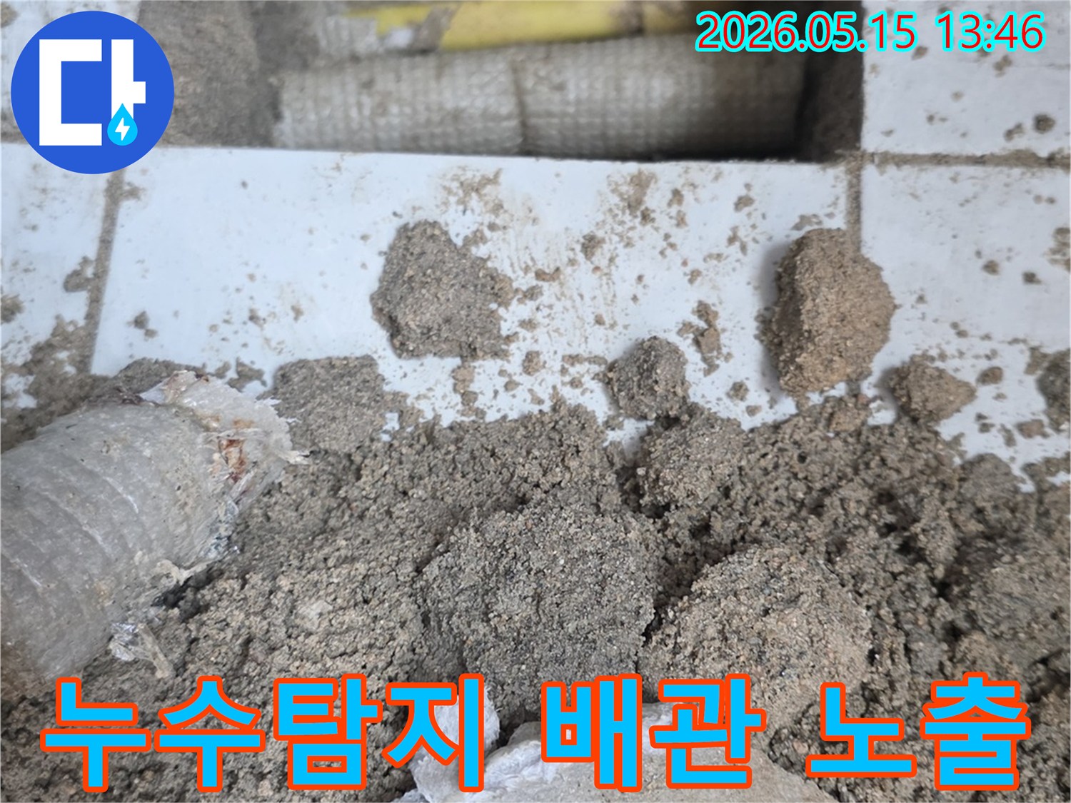 누수 공사 현장에서-바닥을 개방하여-드러난 배관과-주변의 흙더미-그리고-파손된 타일 조각들입니다