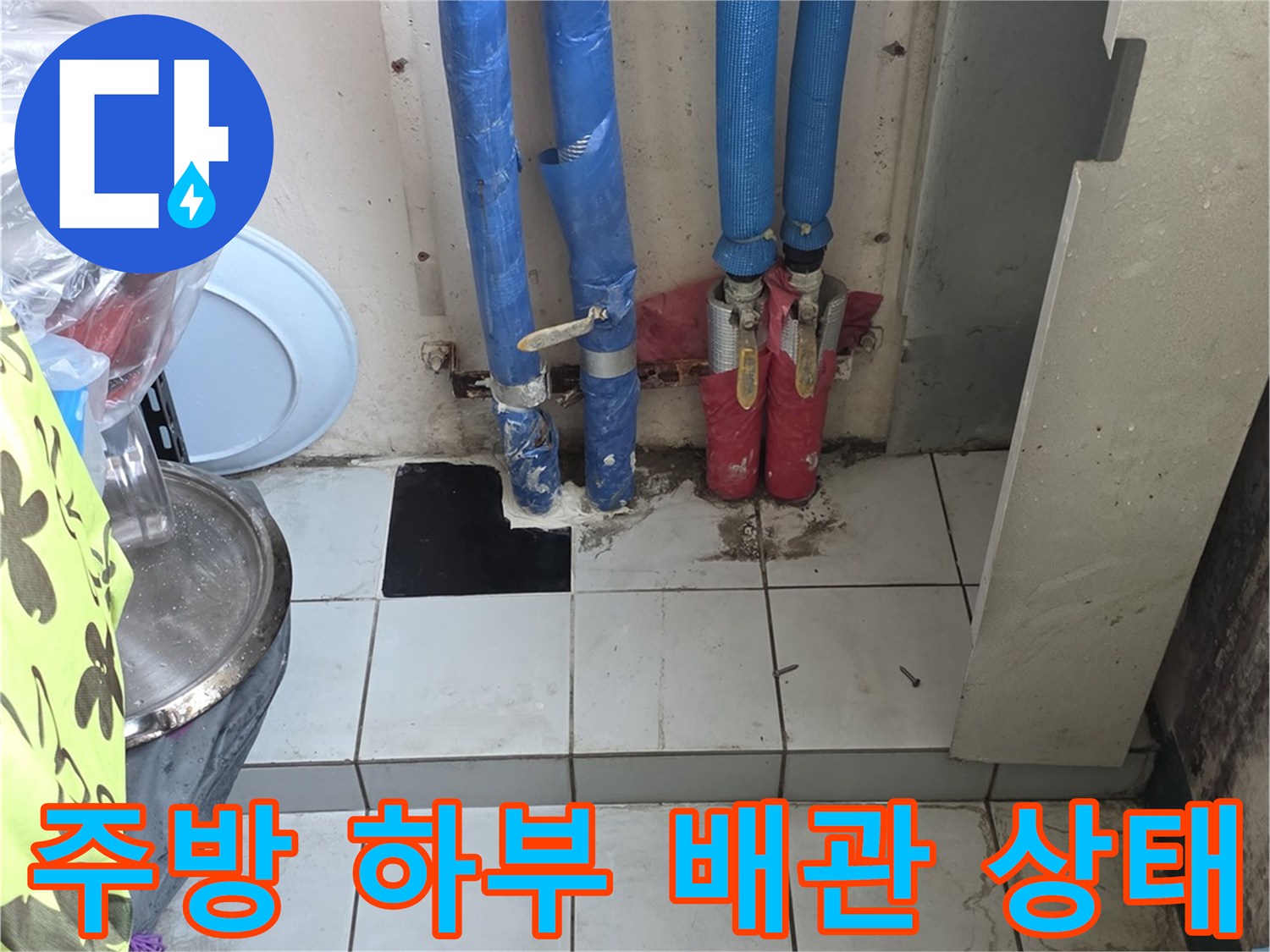 싱크대 아래 파란색 보온재가 있는 배관과 타일 벽면의 모습