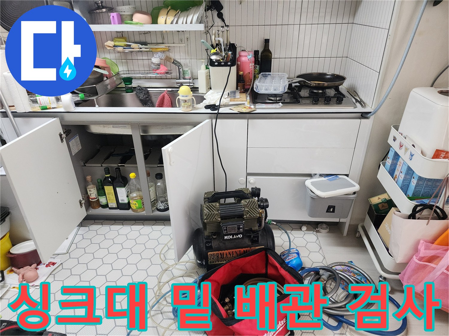 주방 싱크대 아래쪽의 배관 연결 부위와 점검 중인 장비 모습