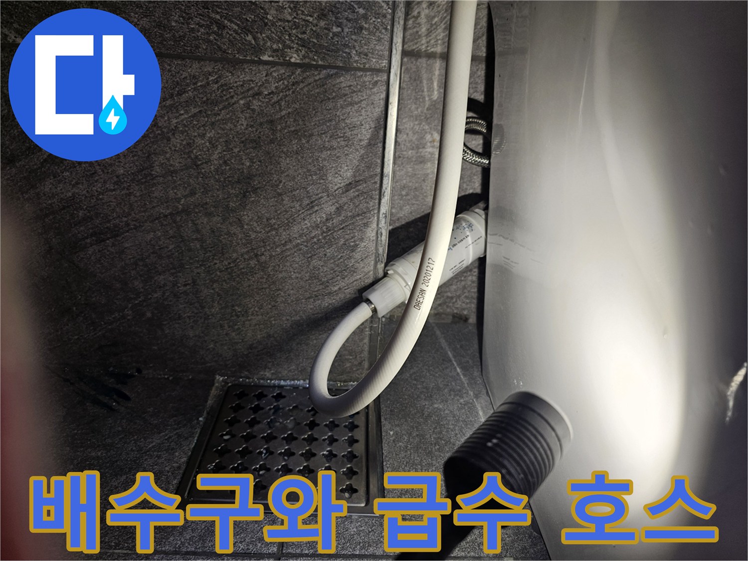 격자형 배수 덮개와 흰색 변기 급수 호스가 연결된 모습