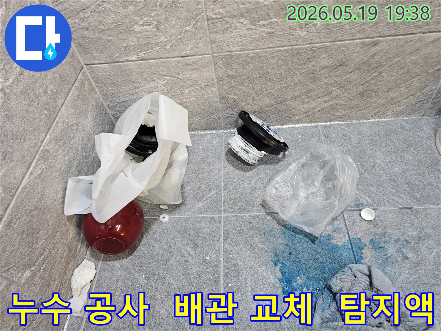 누수 공사 현장에서-파란색 탐지액으로 확인된 누수 지점과-교체된 배관 부품들이 바닥에 놓여 있습니다