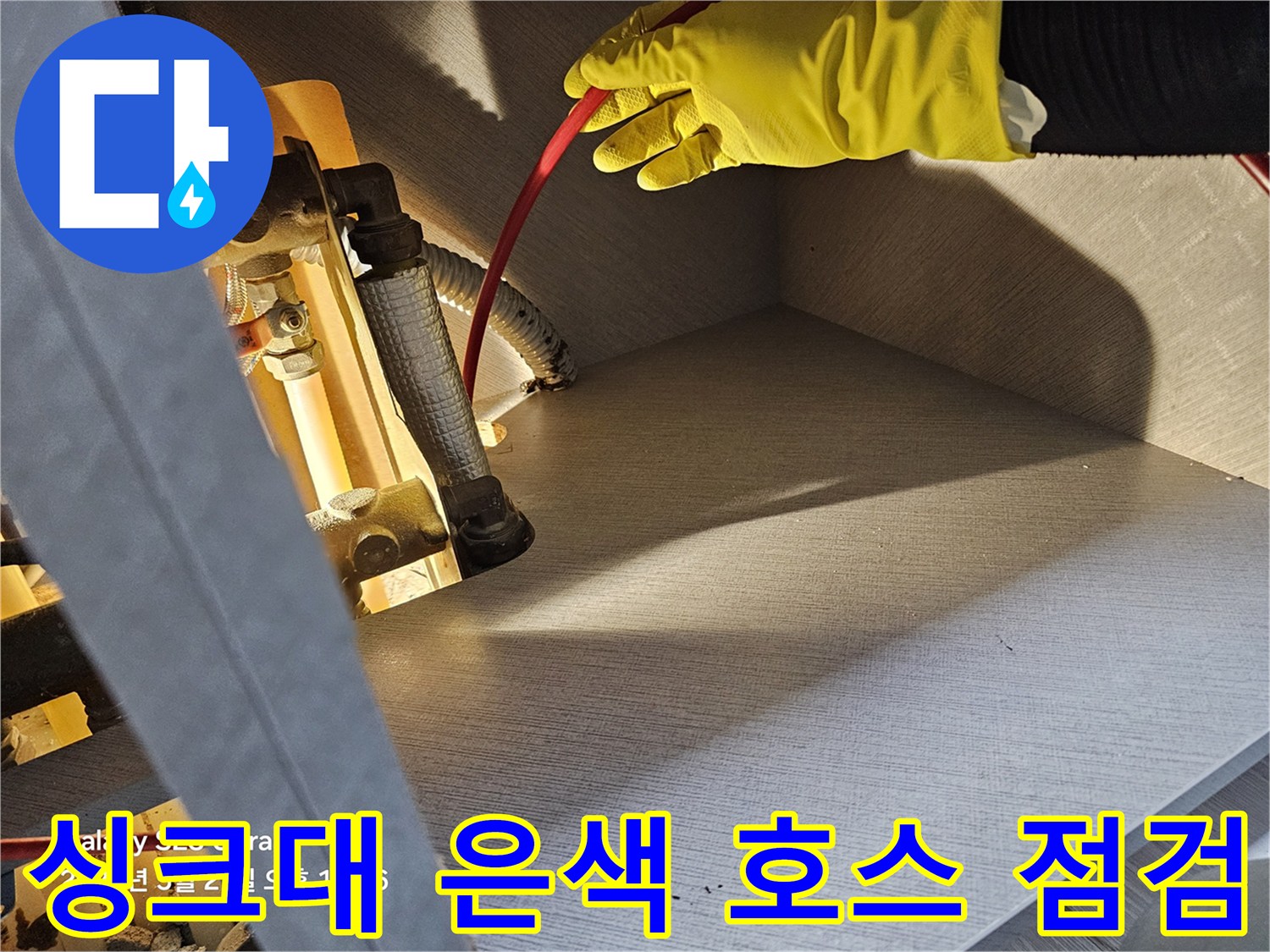 노란 장갑을 낀 작업자가 - 싱크대 하단 금속 배관을 만지는 장면