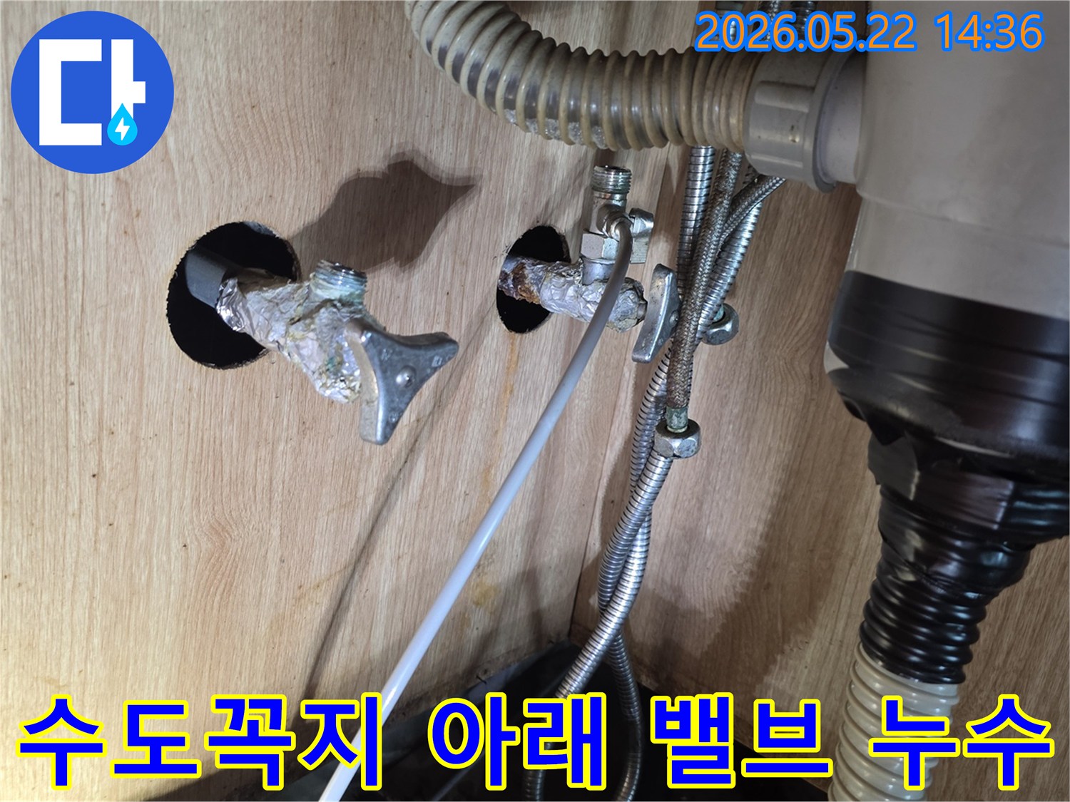 싱크대 수도꼭지 아래에 위치한 밸브 연결부에서 물이 새는 현장을 담은 사진입니다