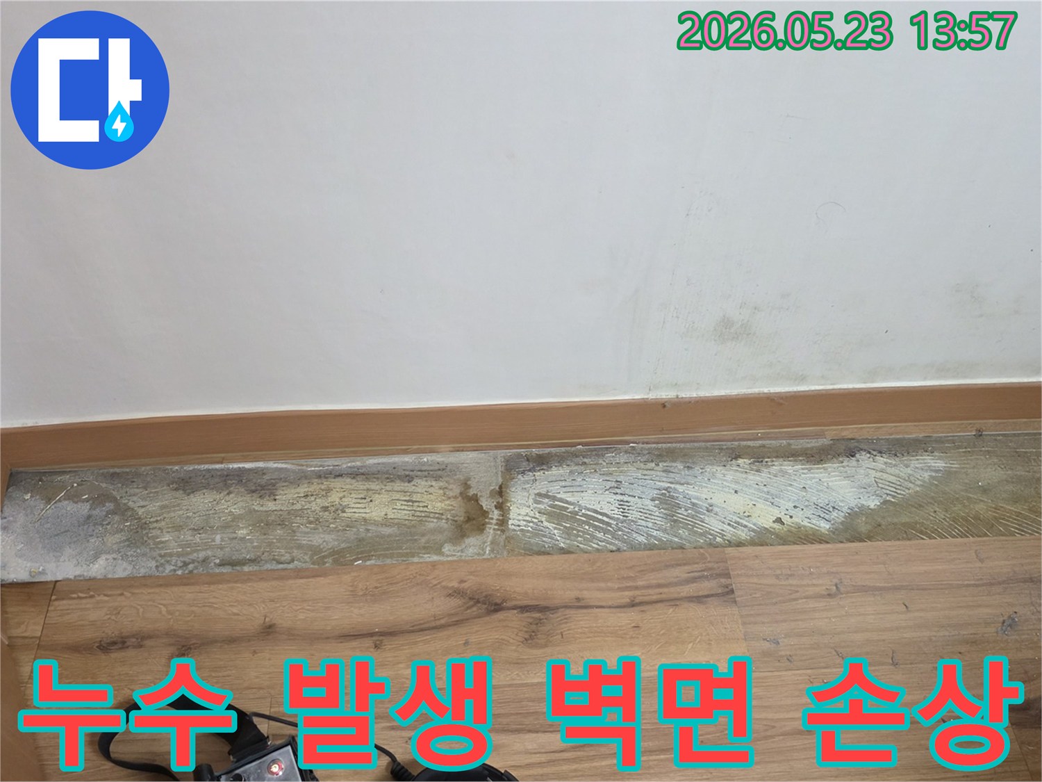 누수 탐지 장비가 놓인-바닥과 함께-벽 하단에-진행된-물기와-곰팡이로 인한-손상을-보여주는-벽면 클로즈업 사진