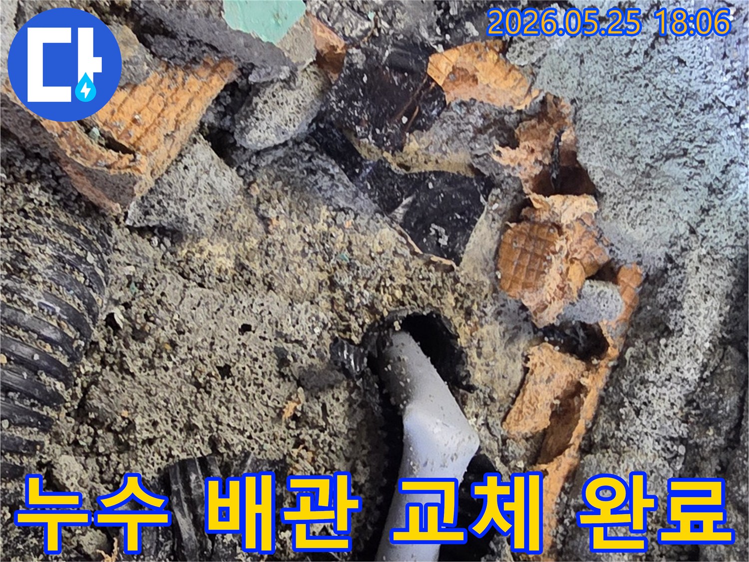 파쇄된 바닥 아래에서 드러난 젖은 배관과 주변의 흙-콘크리트 조각들은-누수 수리를 위한 배관 교체 작업을 보여줍니다.