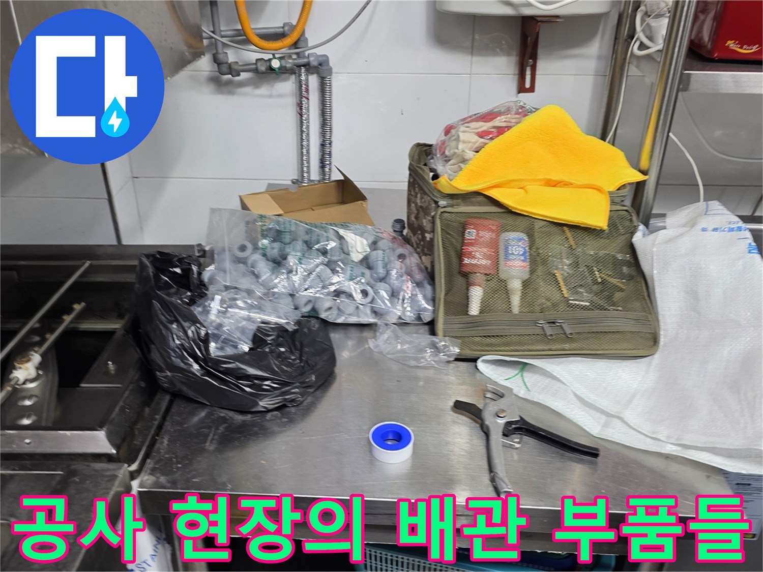 스테인리스 작업대 위에 놓인 다양한 배관 연결용 금속 부품과 수공구